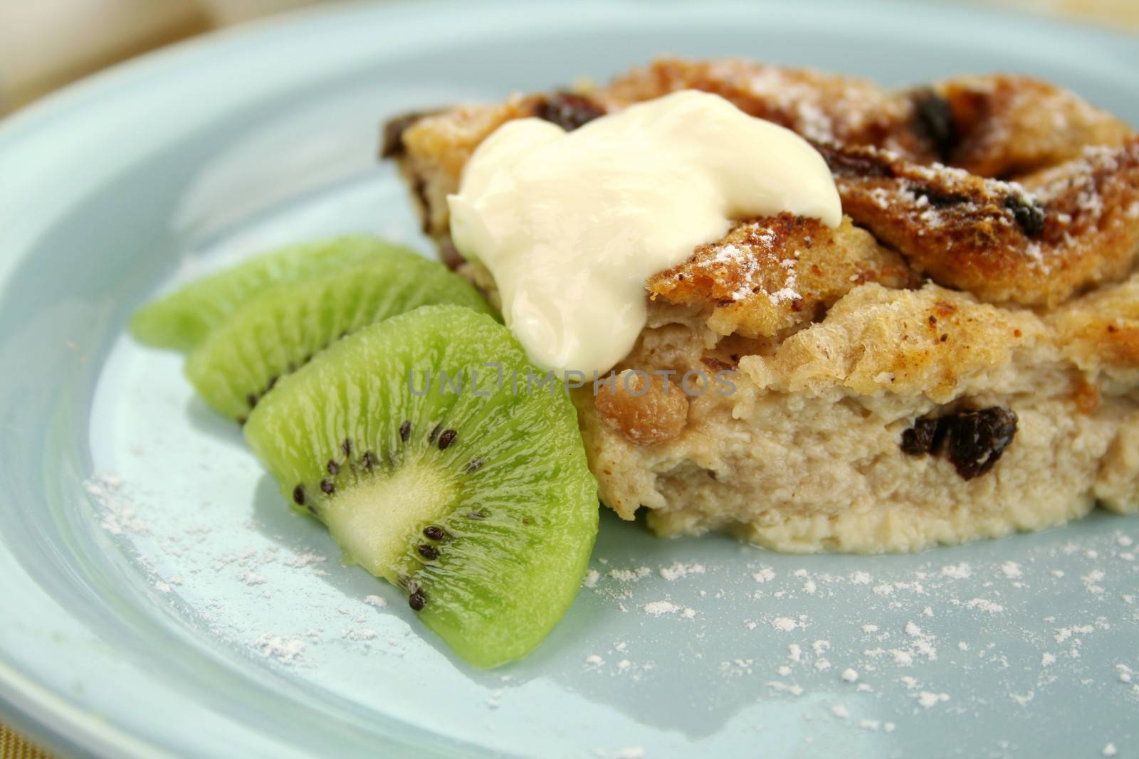 Delicious bread and butter pudding dessert with kiwi fruit and cream.