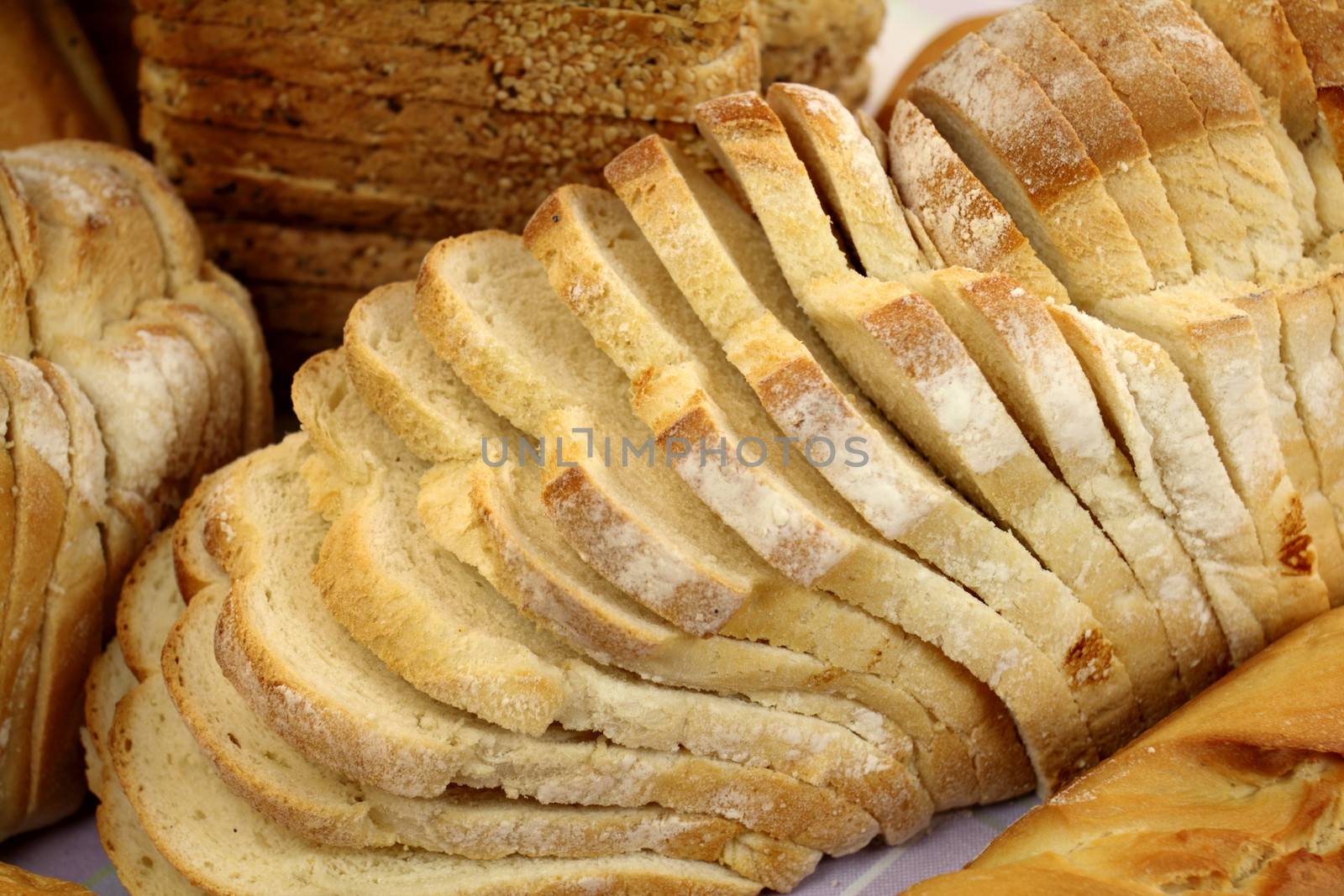 Background of loaf of fresh baked sliced bread amongst other types of bread.