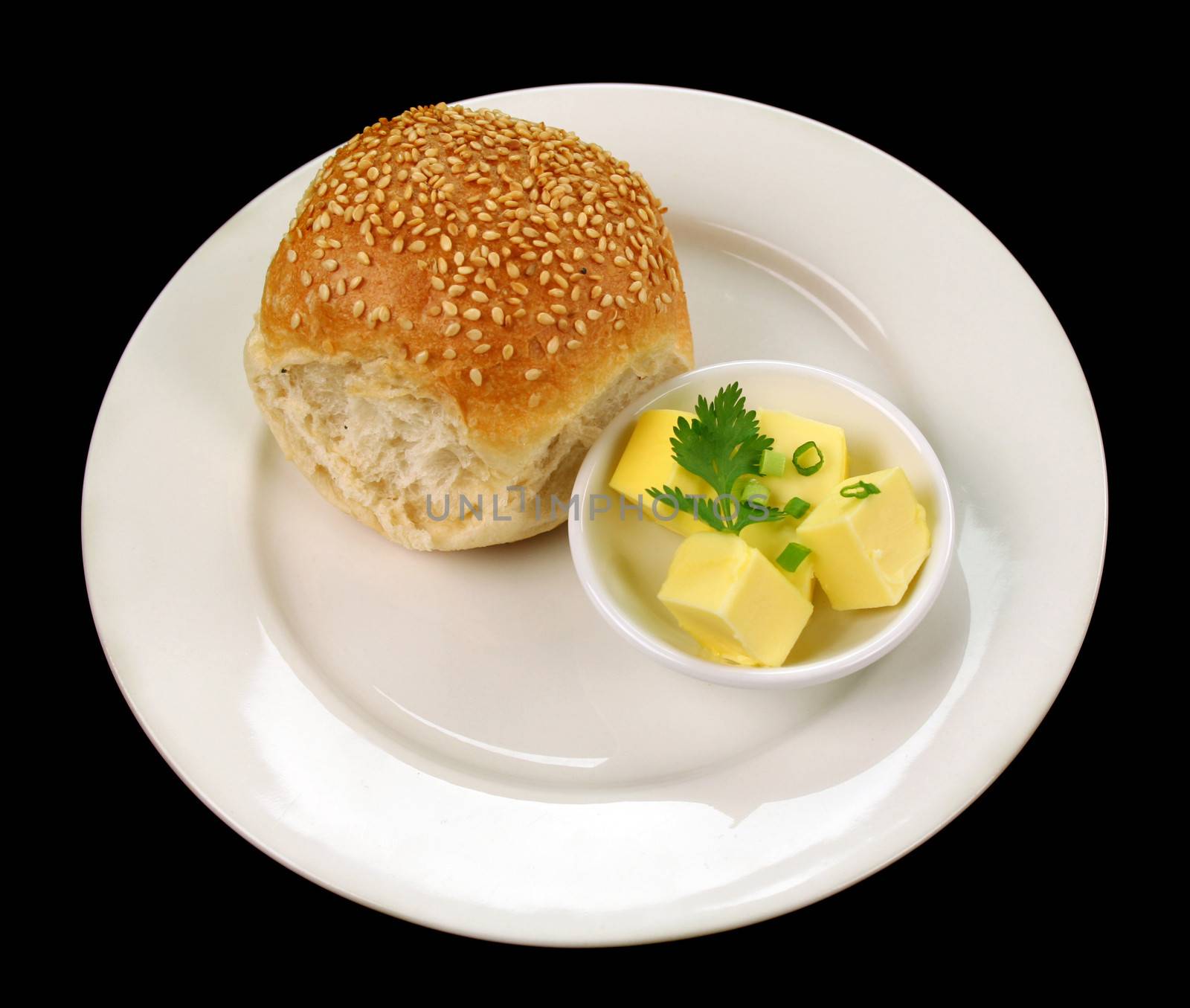 Dinner bread roll with dish of butter with green garnish.