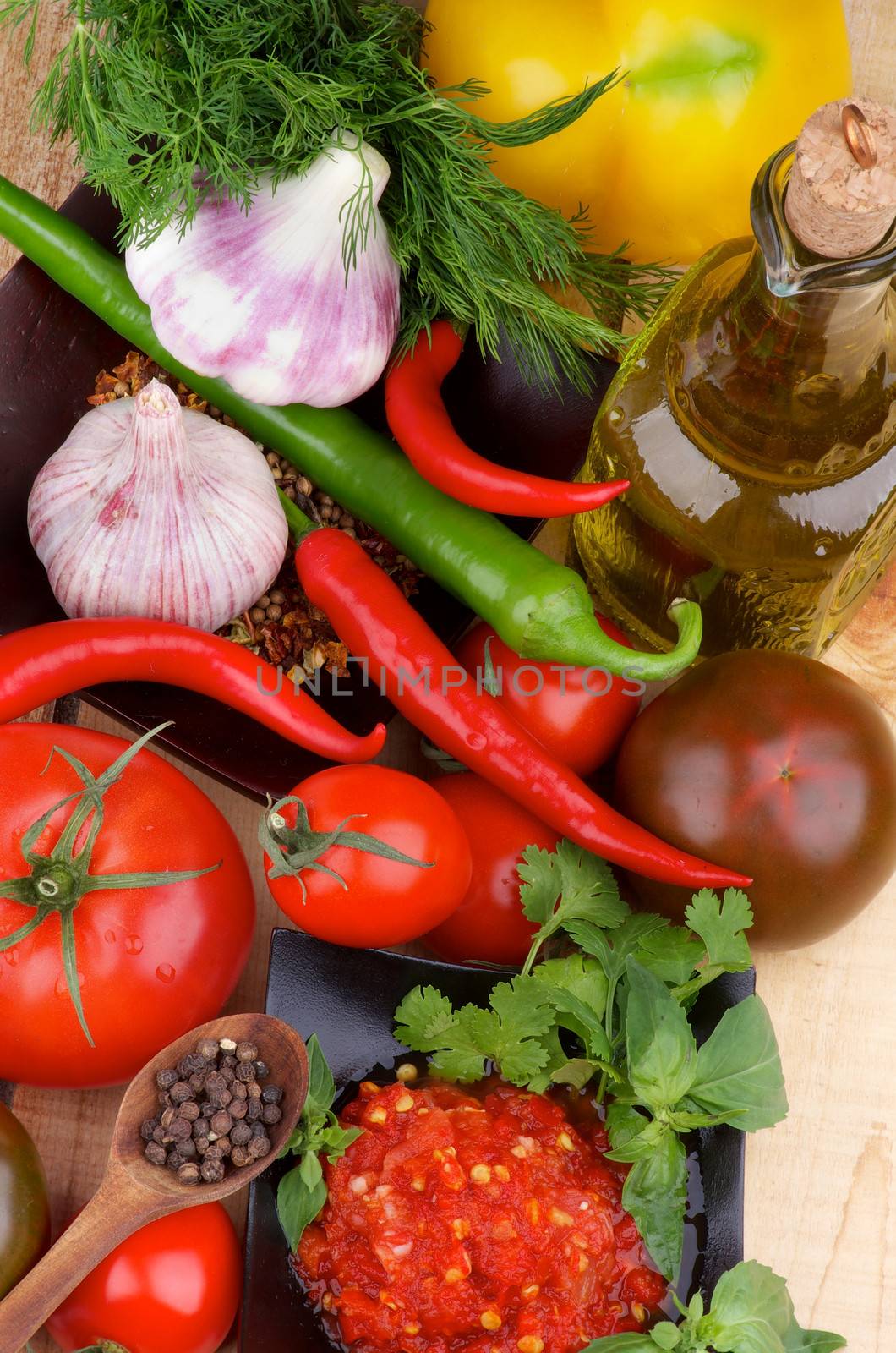 Arrangement of Bruschetta Sauce in Black Bowl with Tomatoes, Garlic, Chili Peppers, Dill, Peppercorn in Wooden Spoon and Olive Oil in Glass Bottle on Wooden background. Top View