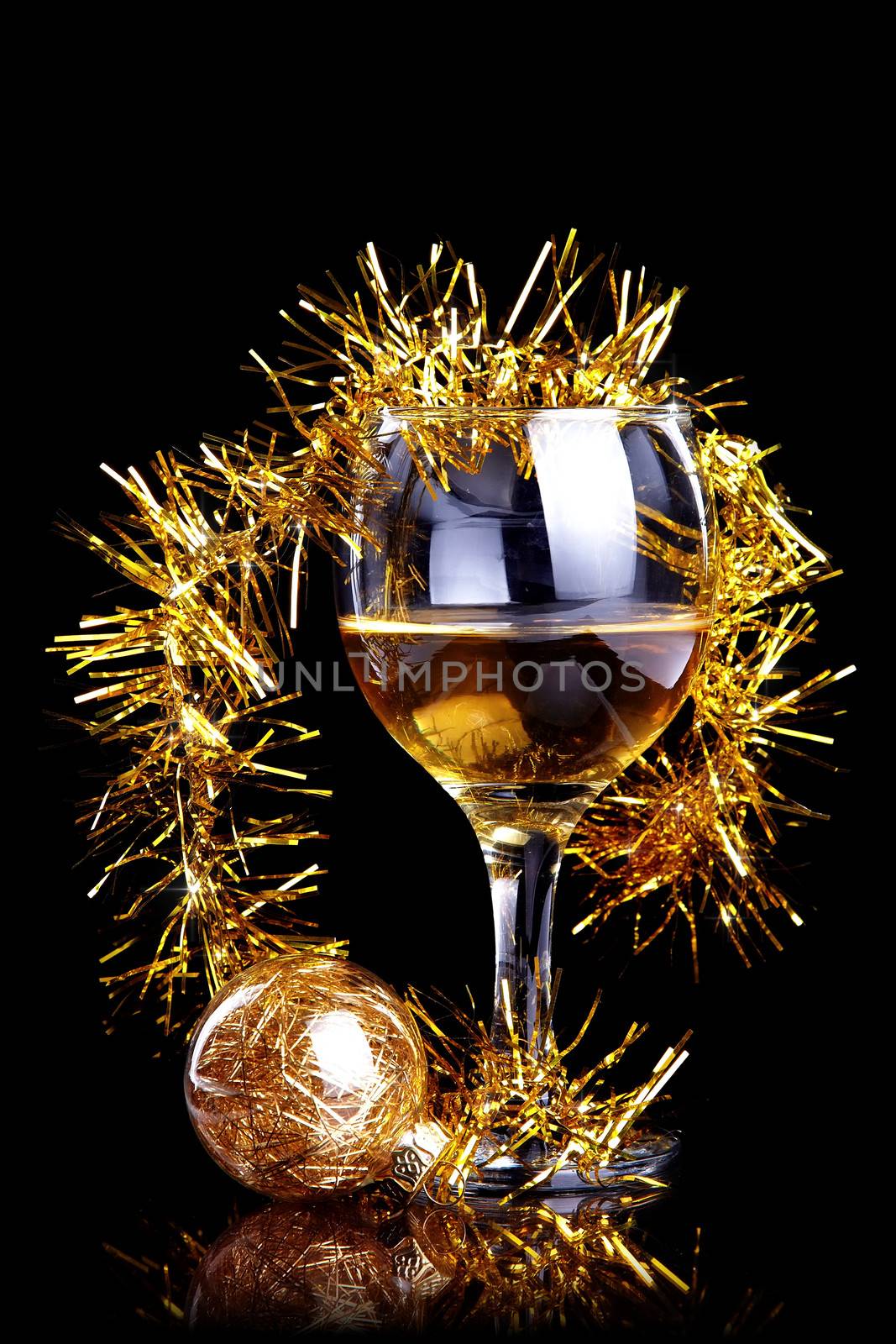 Glass with drink, a Christmas ball and tinsel on a black background. Glass with alcohol and a Christmas ball.