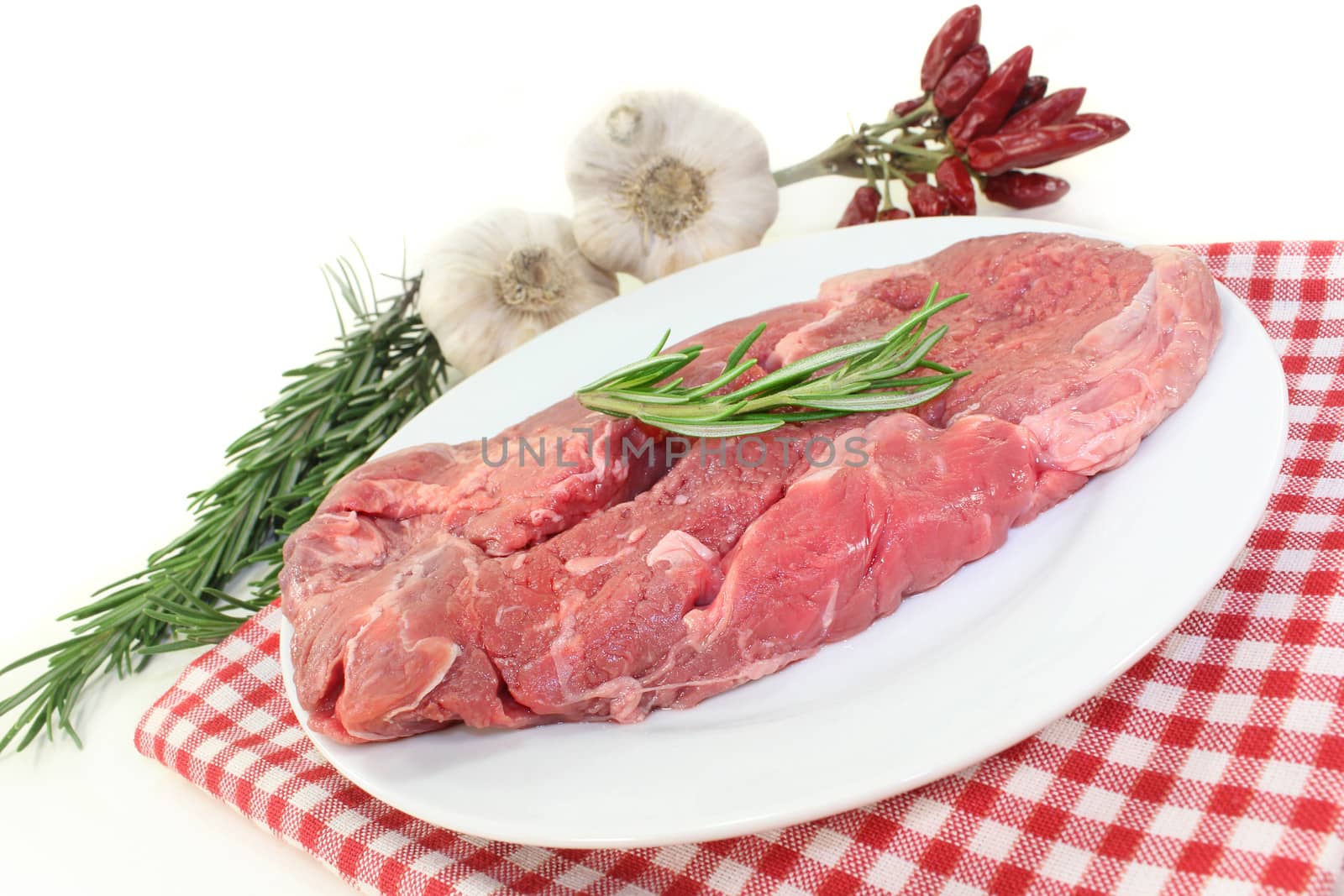 a piece of raw sirloin steak with rosemary and garlic