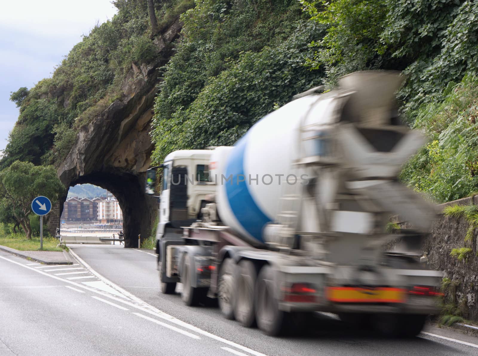 Mixer truck about to go through small tunnel in the rock on a road by the beach
