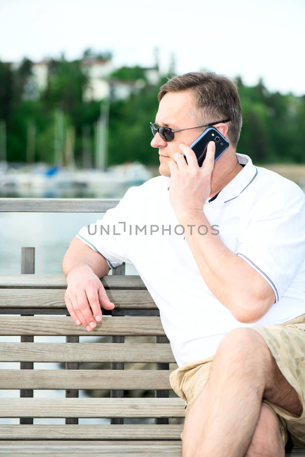 Mature caucasian man with the phone on wooden bench by Nanisimova