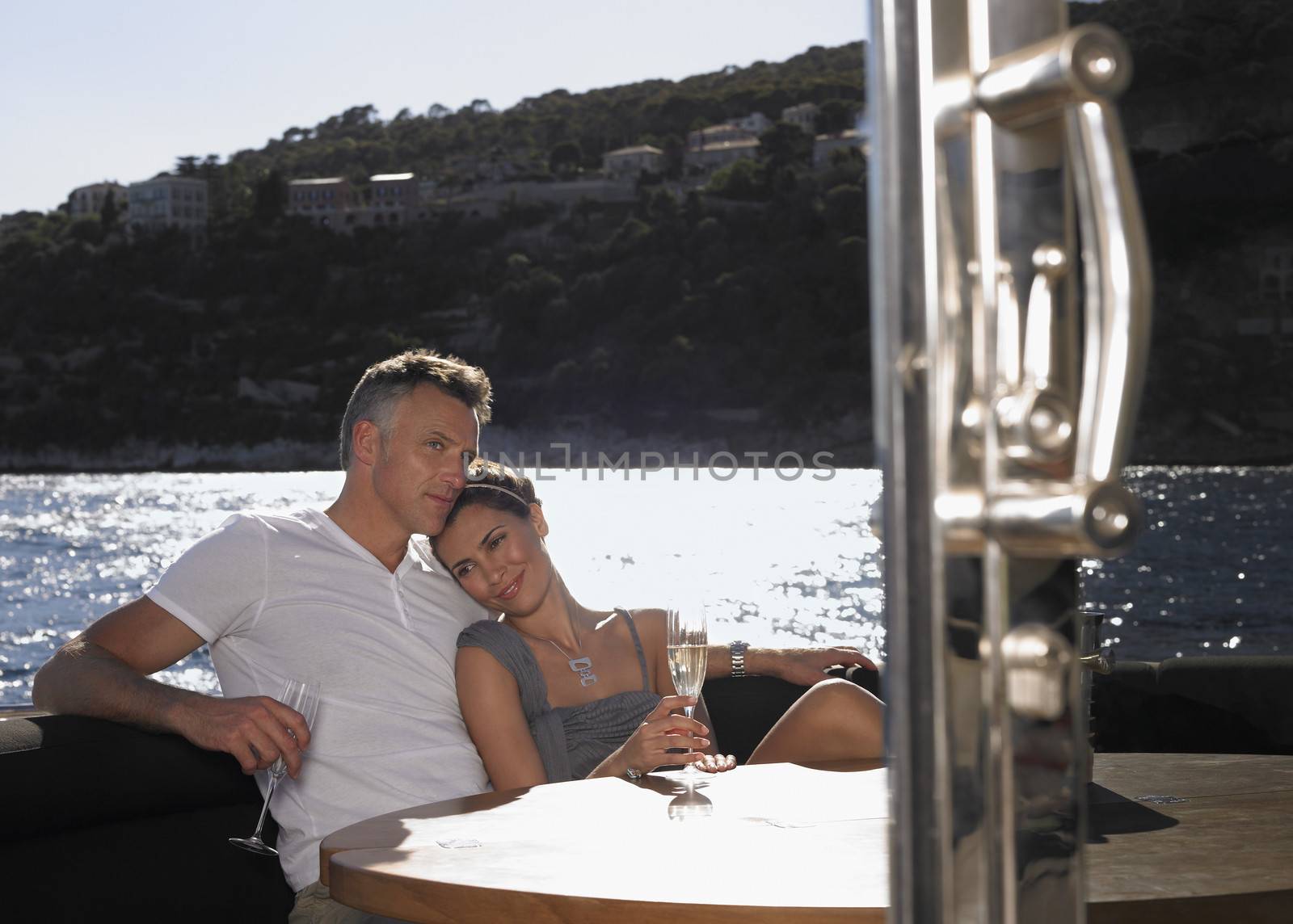 Romantic couple having champagne while sitting at table on yacht by moodboard