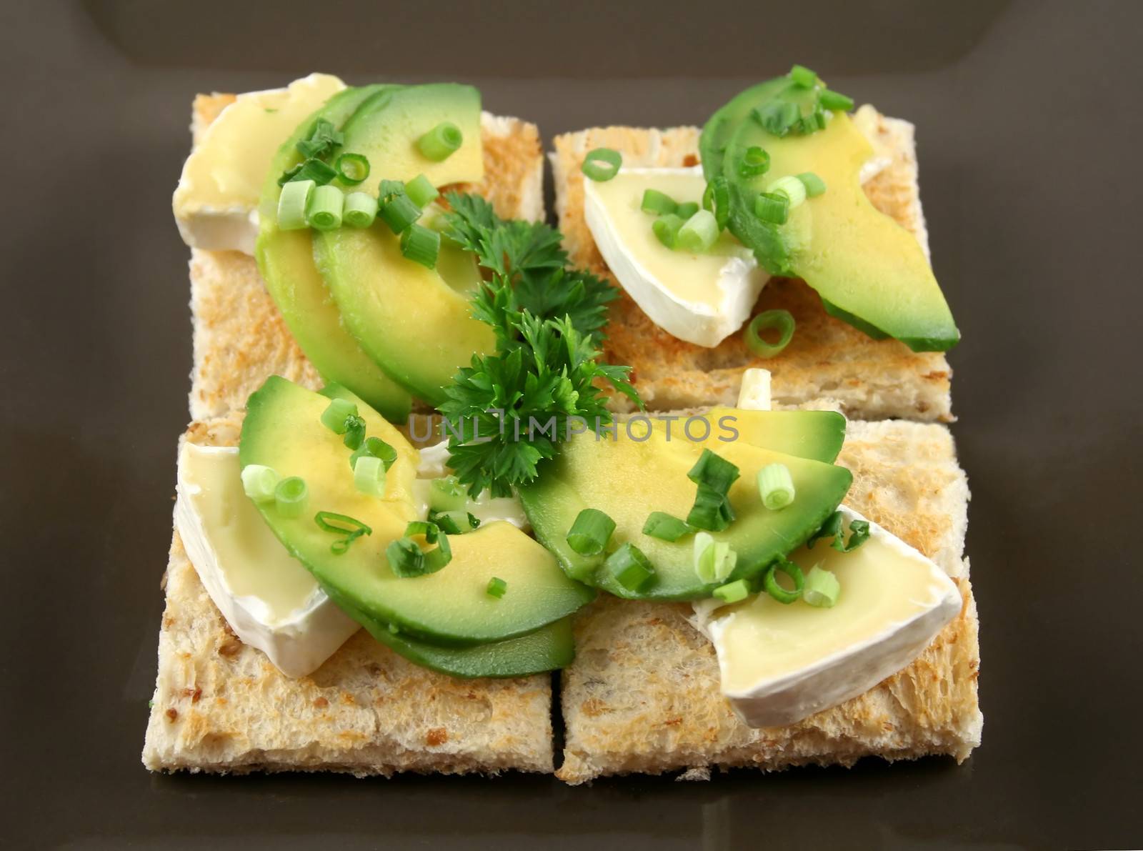 Camembert and avocado bites with spring onions on wholegrain squares.