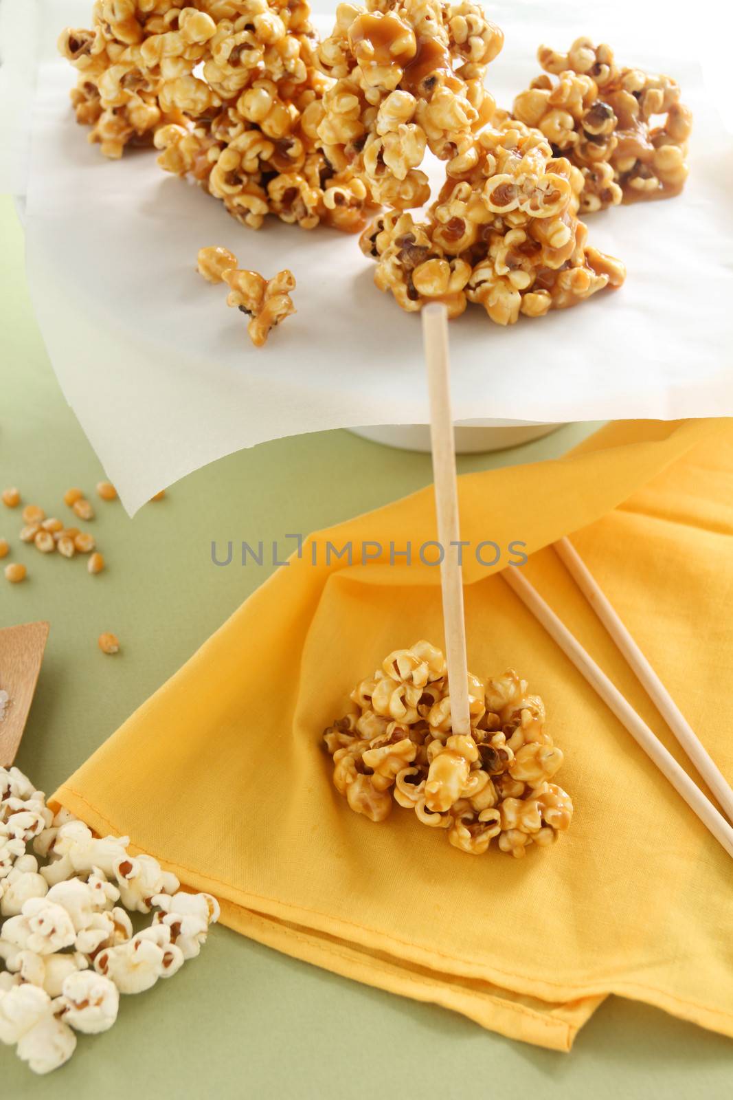 Caramel popcorn on a stick with raw popcorn on the side.