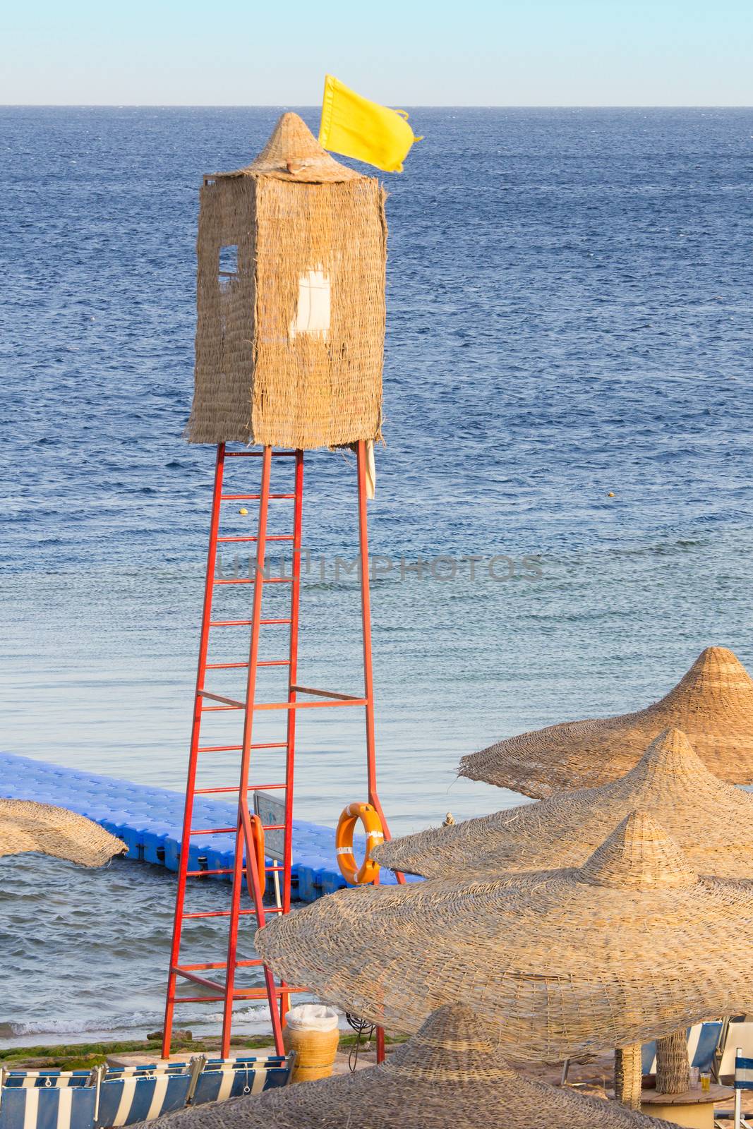 A wicker lifeguard watchtower or lookout tower and yellow flag on a beach.