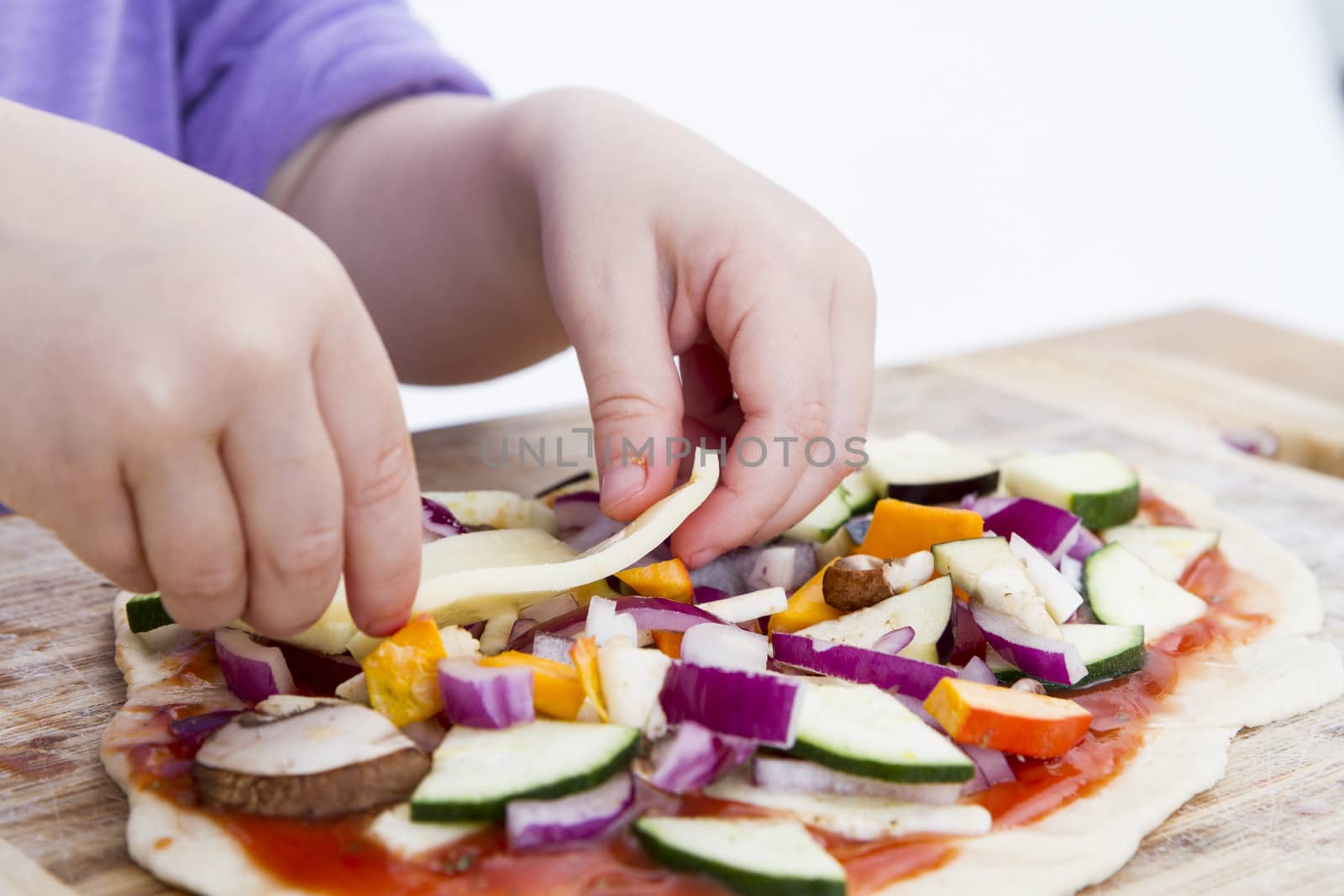 small hands preparing fresh pizza with many vegetables