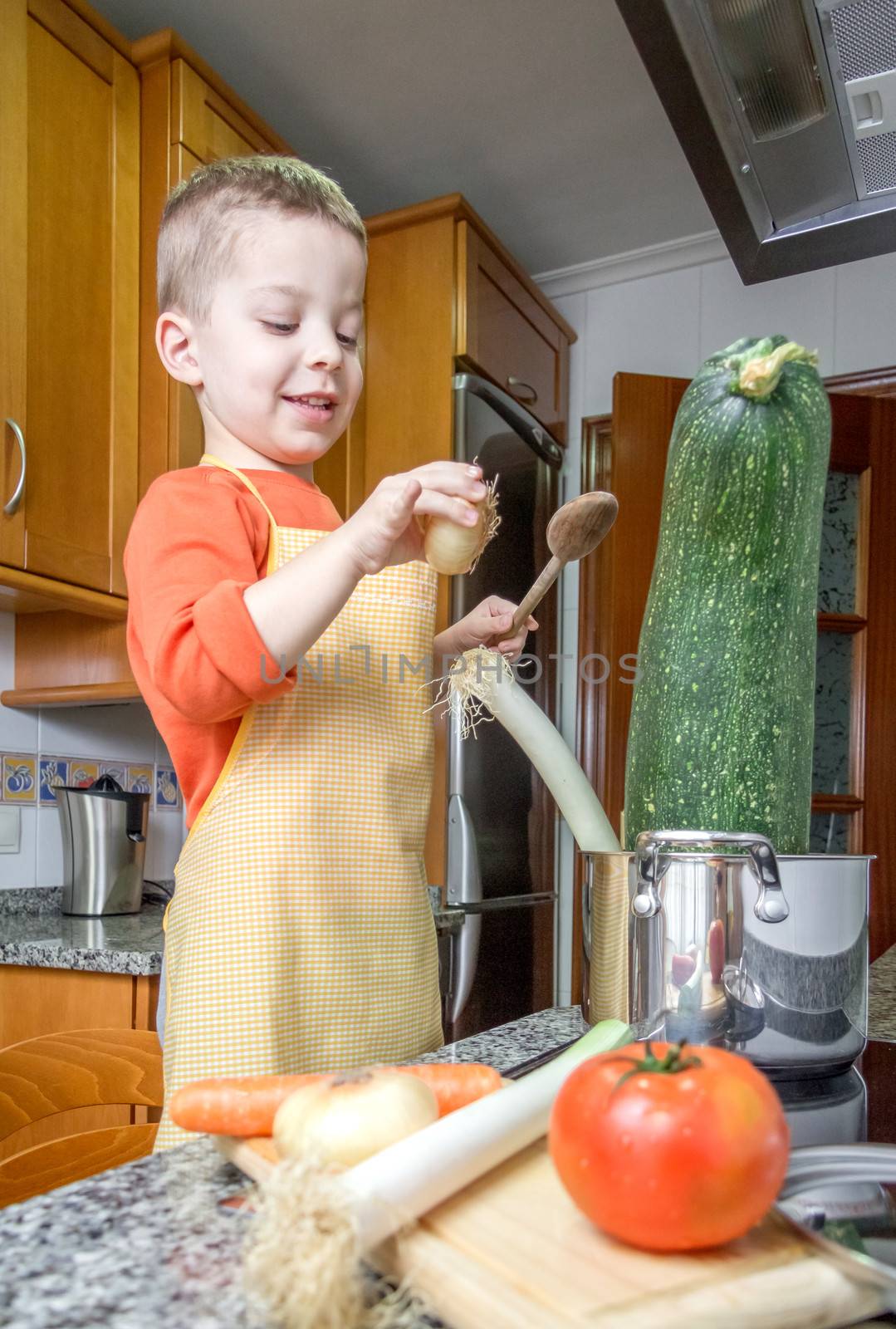 Cute child chef with apron cooking big zucchini and other vegetables in a pot on the kitchen