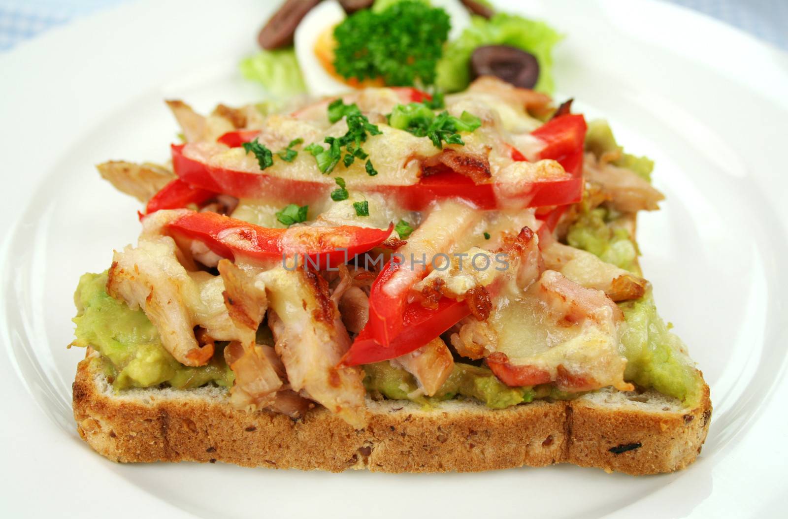 Grilled open chicken sandwich with avocado, peppers and cheese with a side salad.