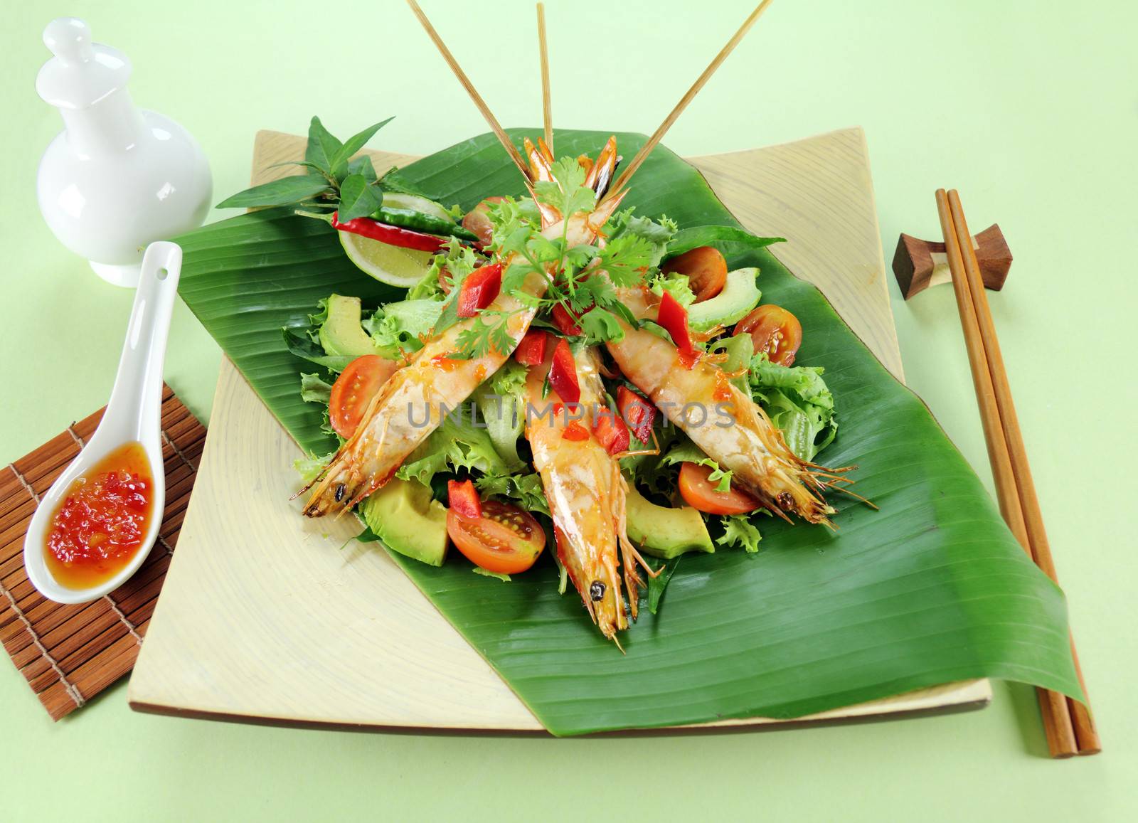 Delicious Asian chilli shrimp skewers a salad on a banana leaf.