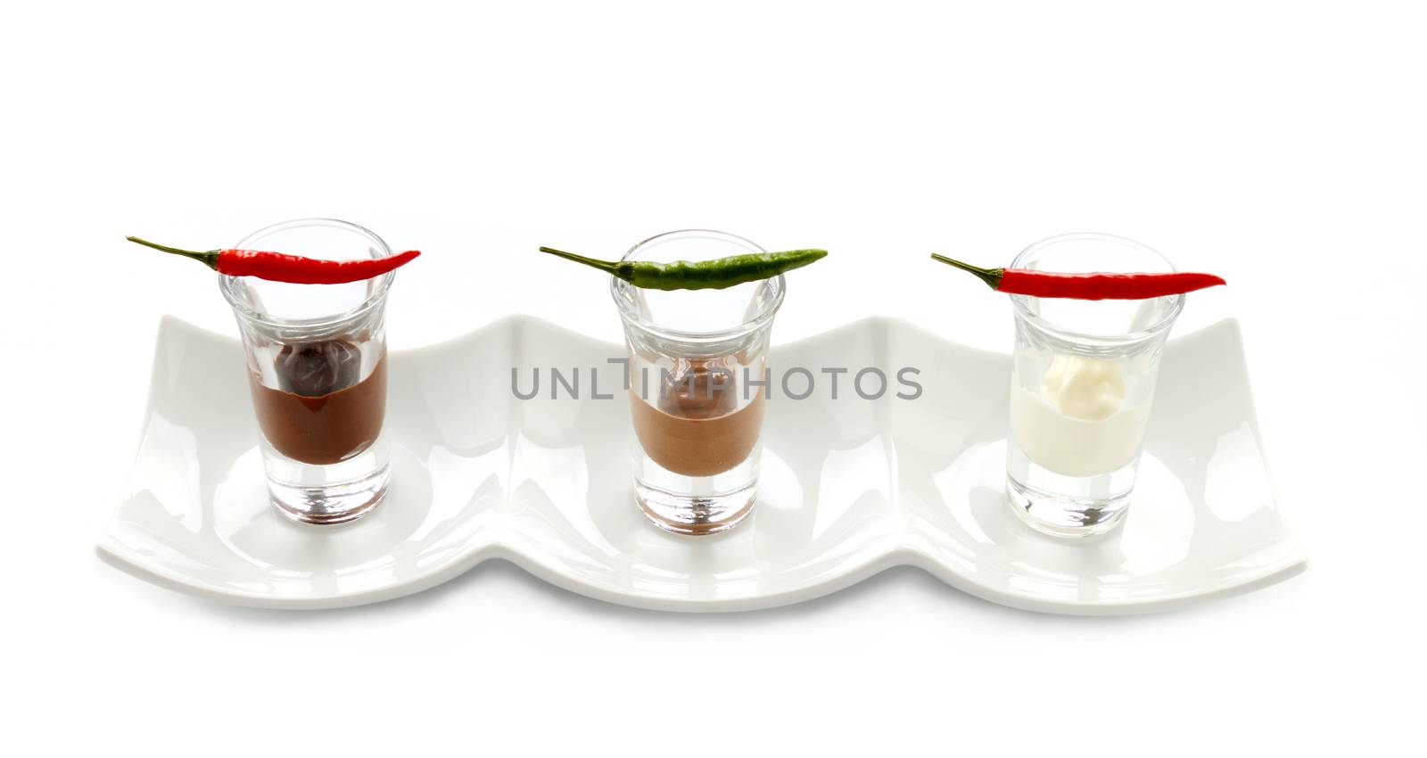 A row of red and green hot chillies lined up in shot glasses with dark, white and milk chocolate.