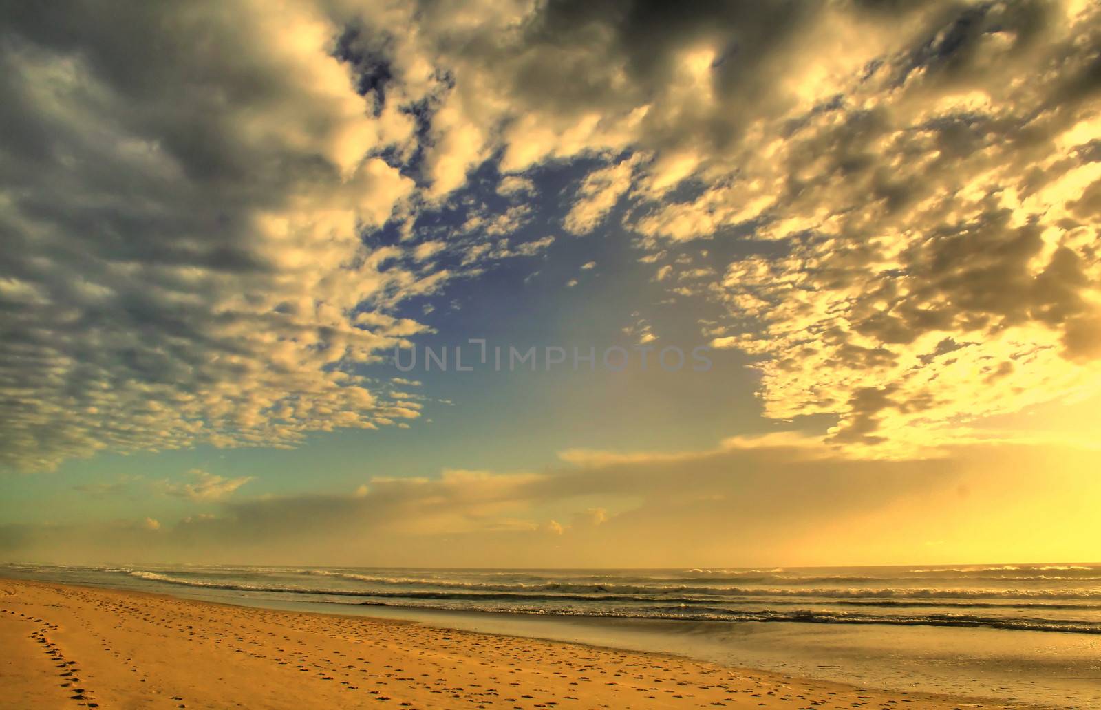 Cloudscape at dawn over beach and rolling waves.