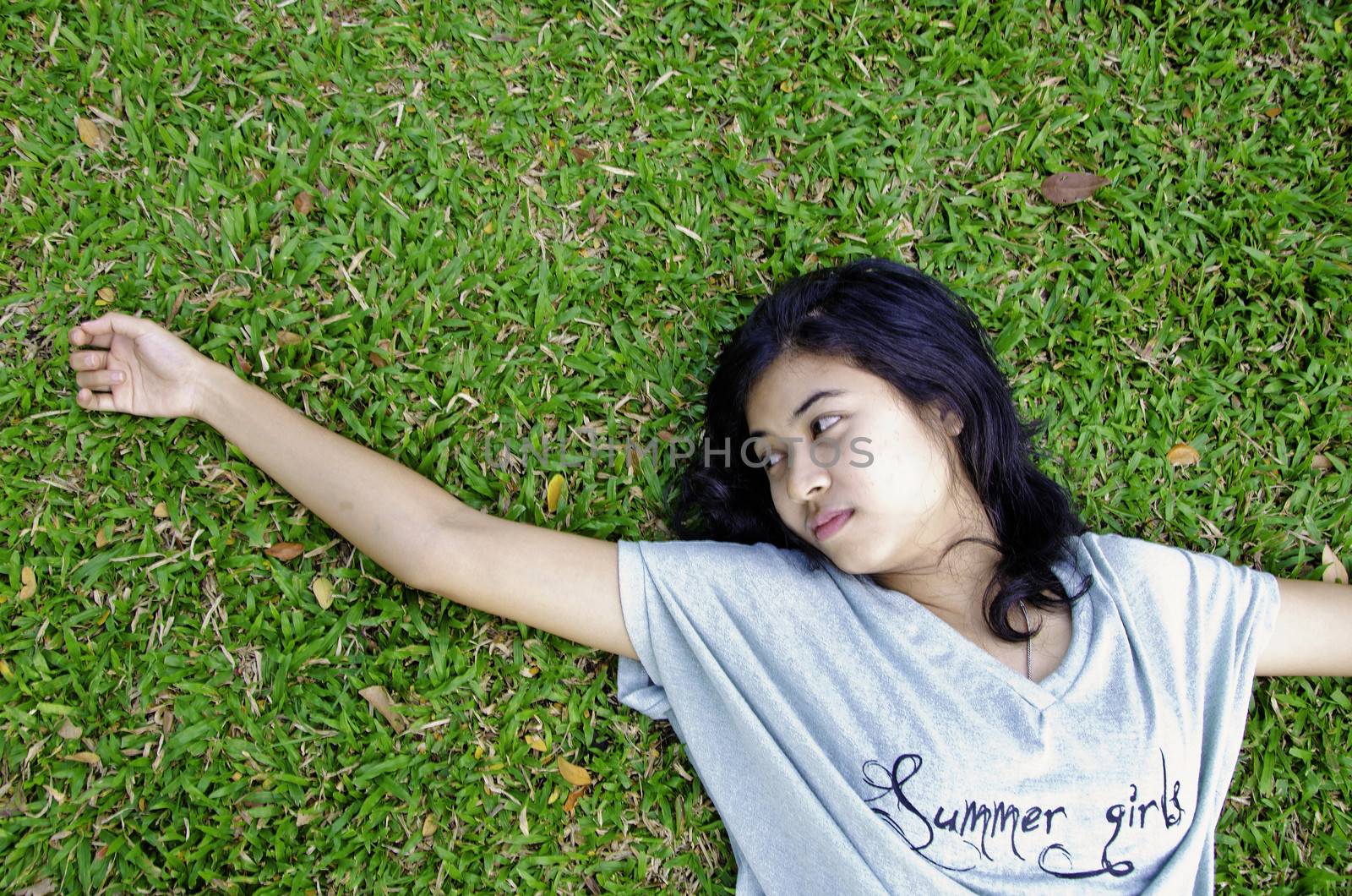 Young asian woman laying in the grass by siraanamwong