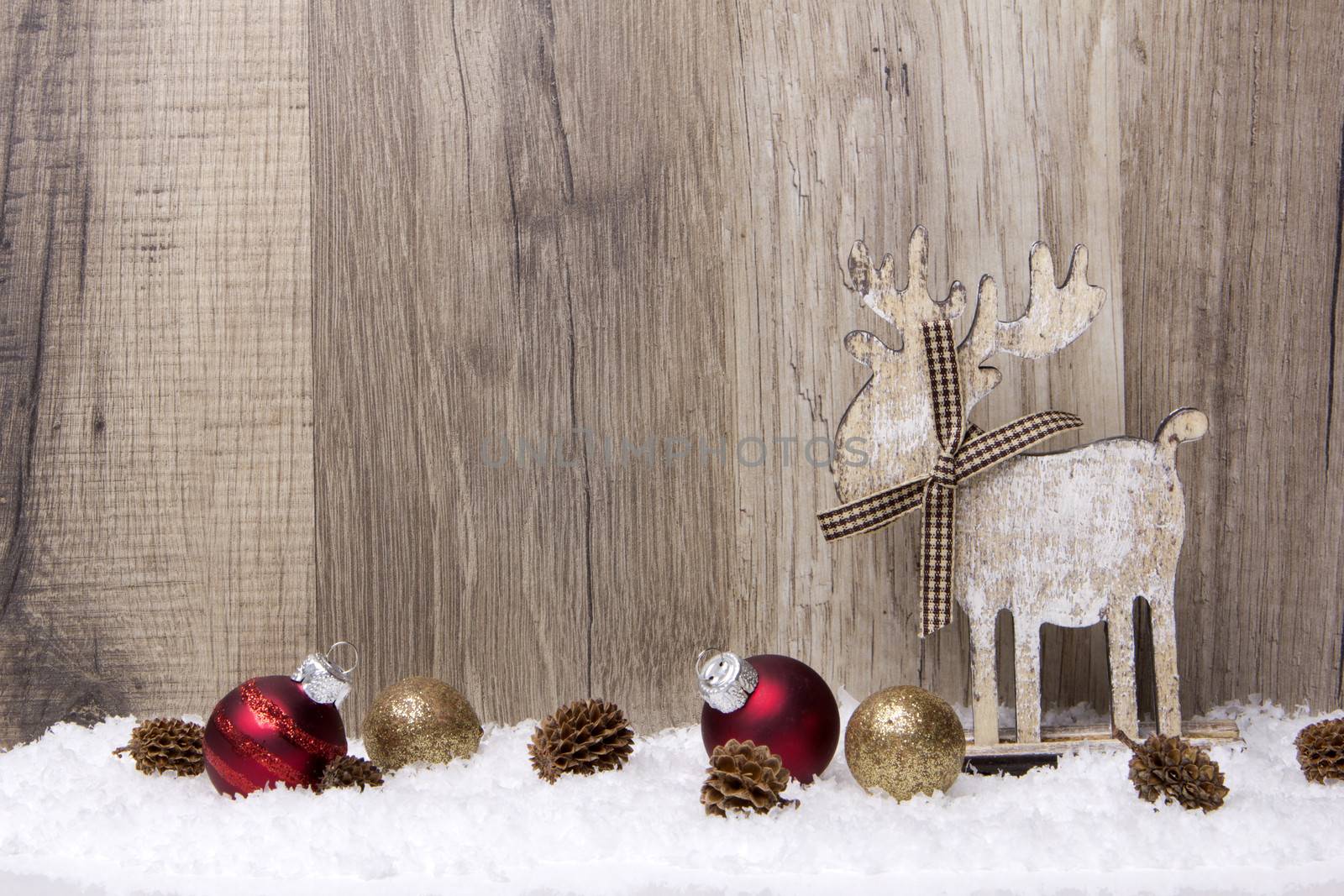 christmas decoration with wood background, snow, elk, christmas baubles gold and red and pine cones 