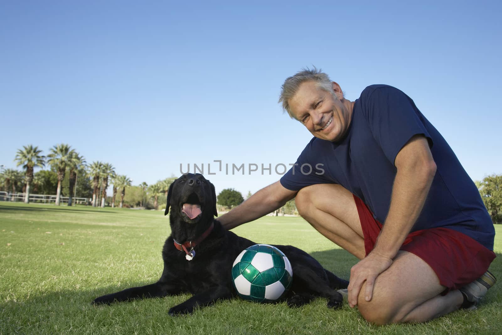 Portrait of a happy senior man with dog and soccer ball in the park by moodboard