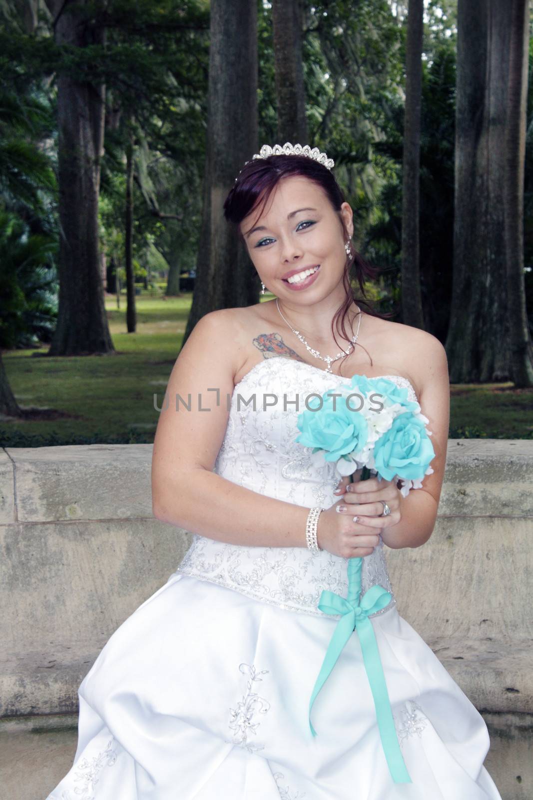 A lovely young bride outdoors wearing her wedding gown and holding her boquet.