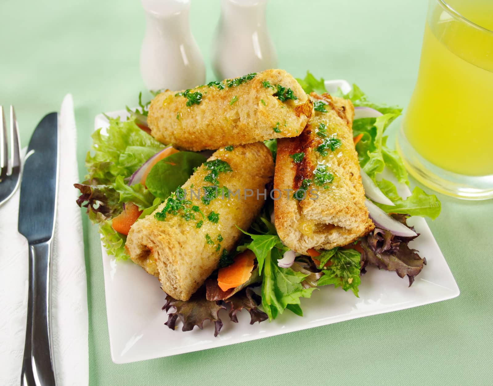 Vegetarian baked corn rolls dripping with parsley butter on a bed of mixed lettuce.