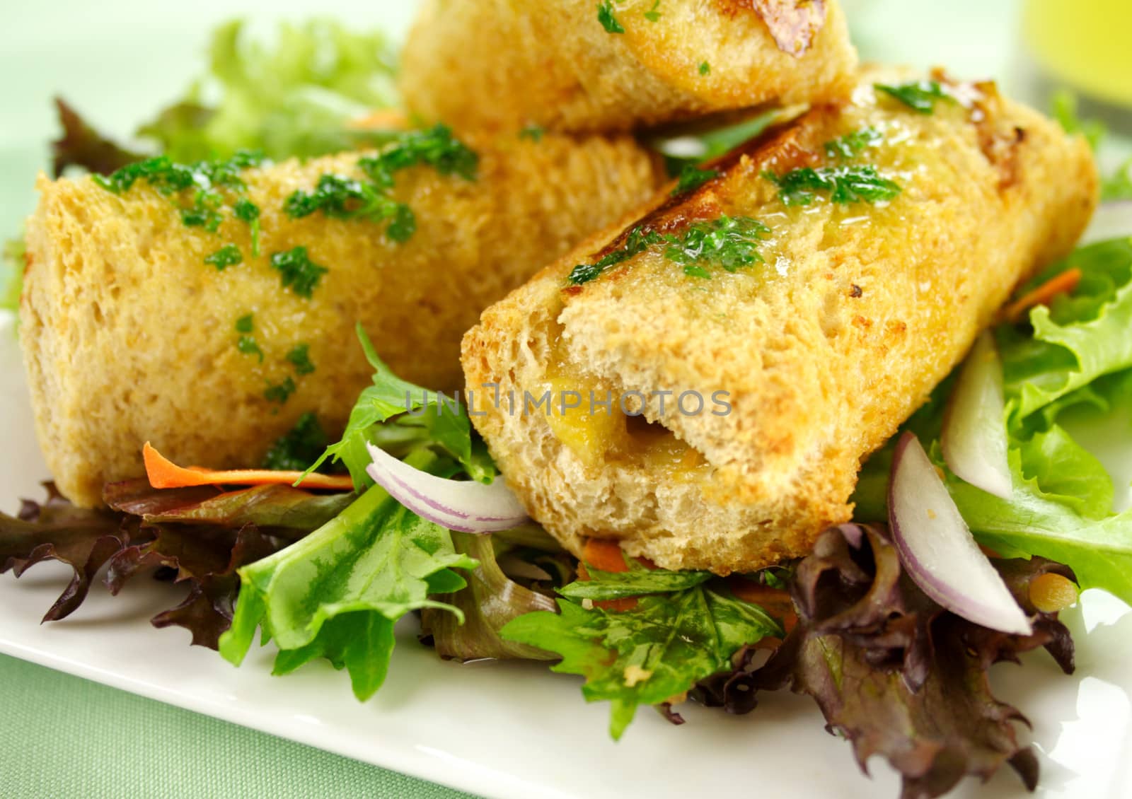 Vegetarian baked corn rolls dripping with parsley butter on a bed of mixed lettuce.