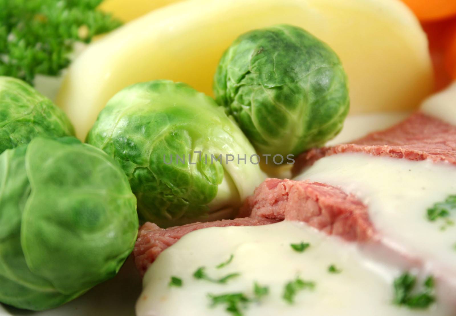 Delicious sliced corn beef with white sauce with brussels sprouts and vegetables.