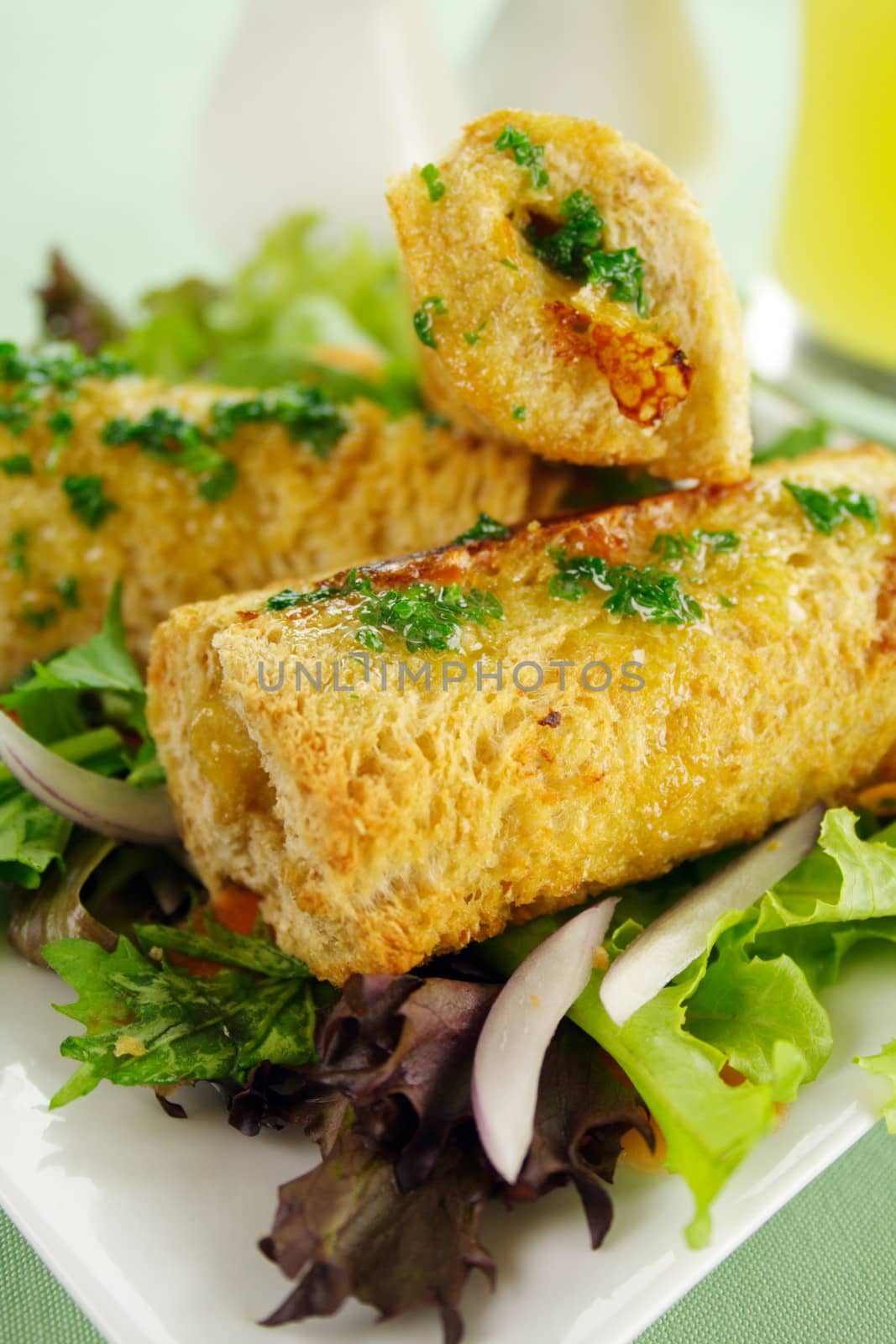 Vegetarian baked corn rolls dripping with parsley butter on a bed of mixed lettuce.