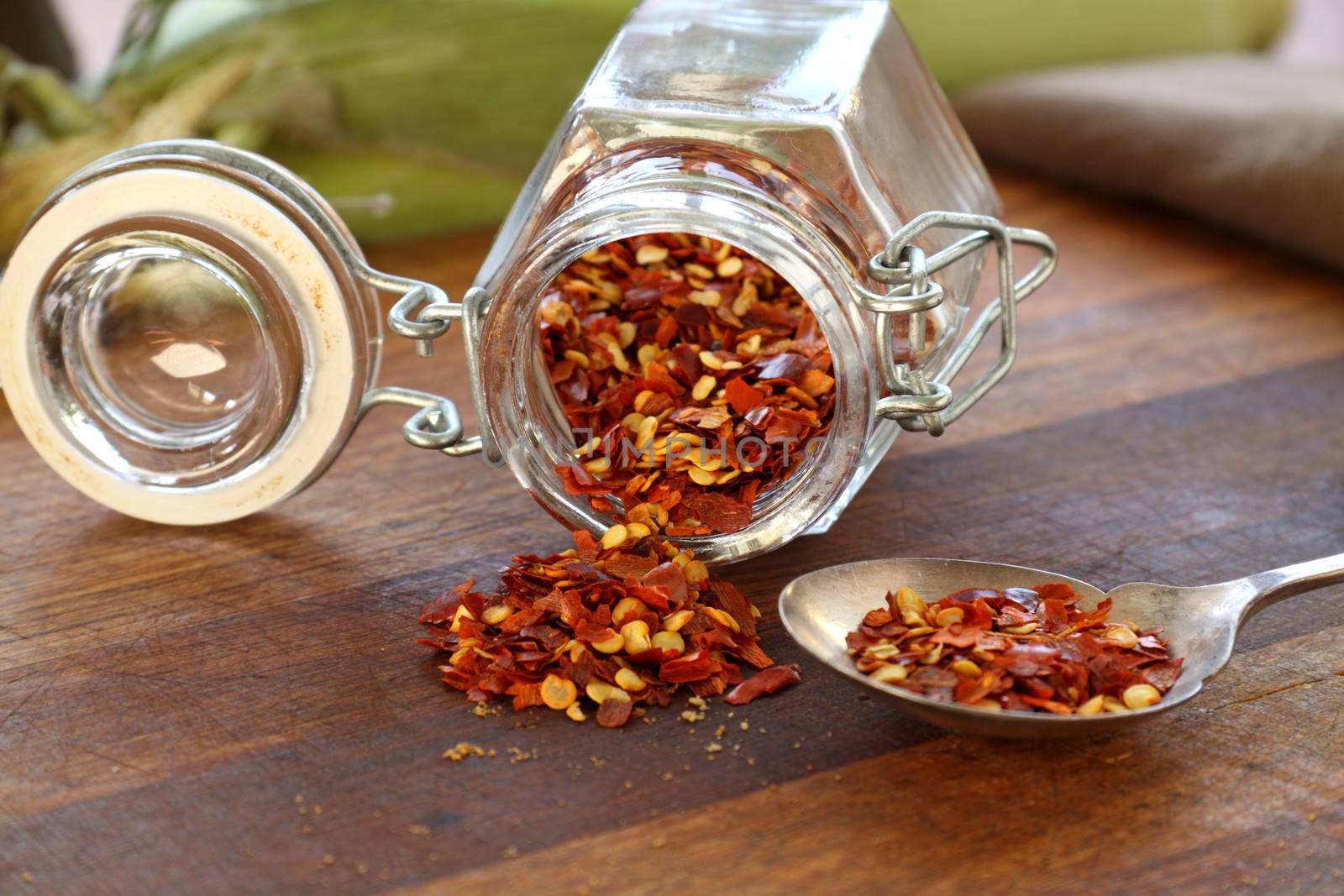 Glass container with dried chili flakes lying on a cutting board.