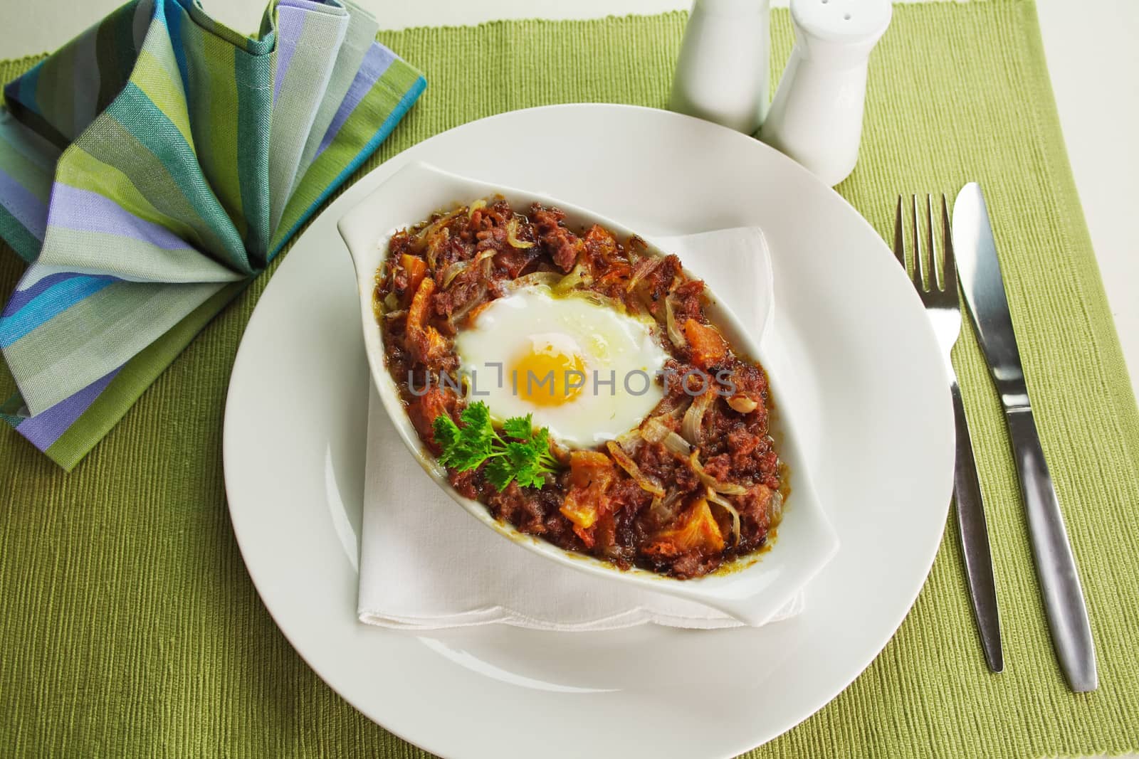 Baked corned beef hash with egg, tomato and onion with parsley.