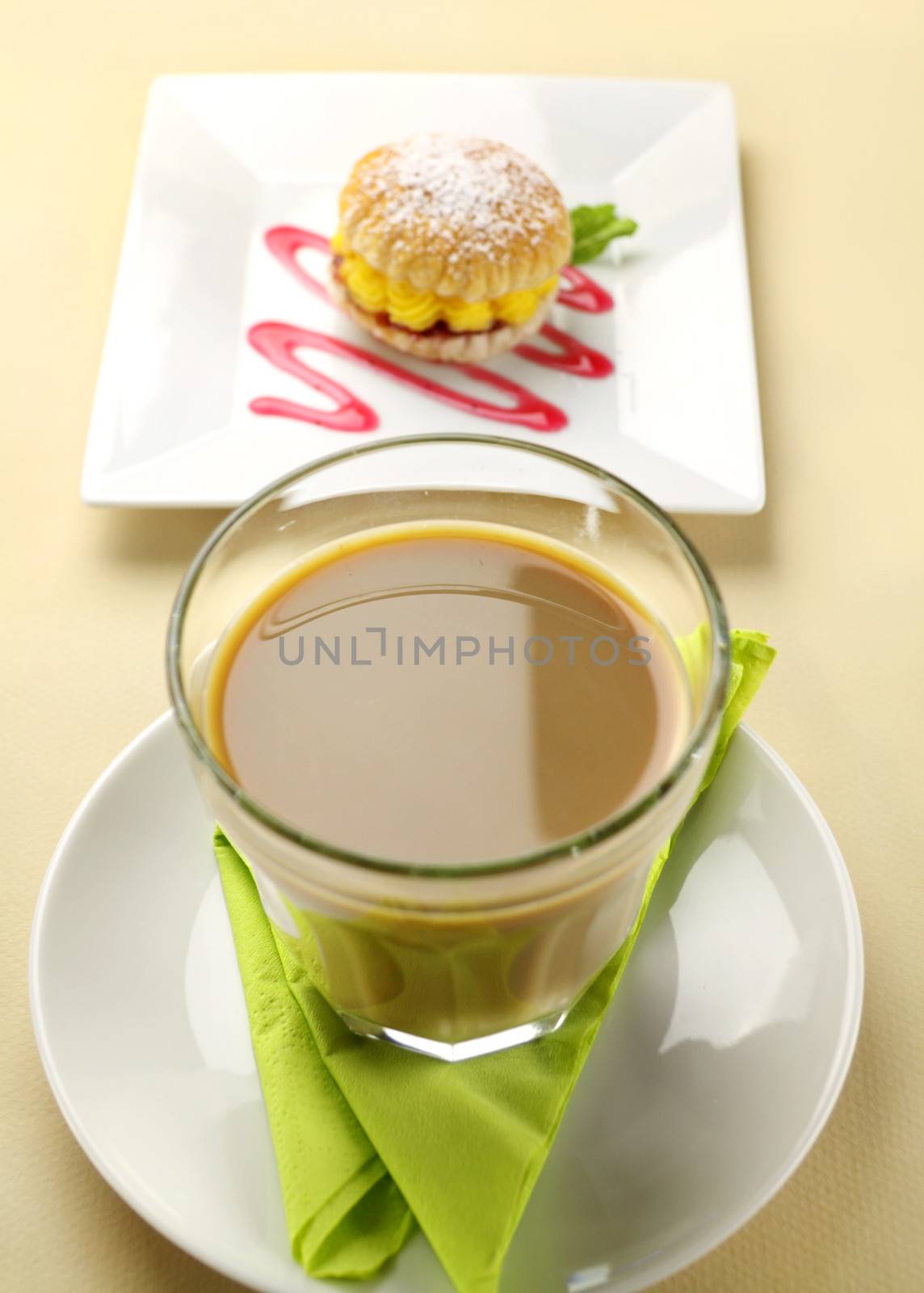Glass of latte with custard tart in the background.