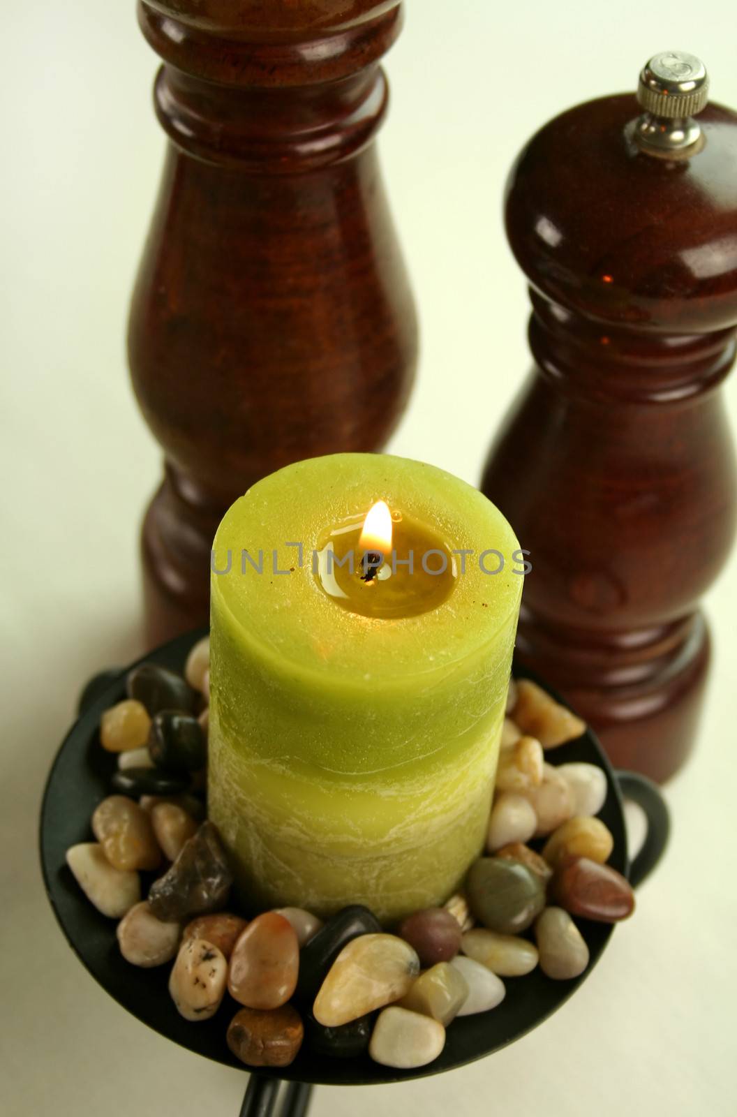 Salt and pepper grinders with a candle set in stones with subdued lighting.