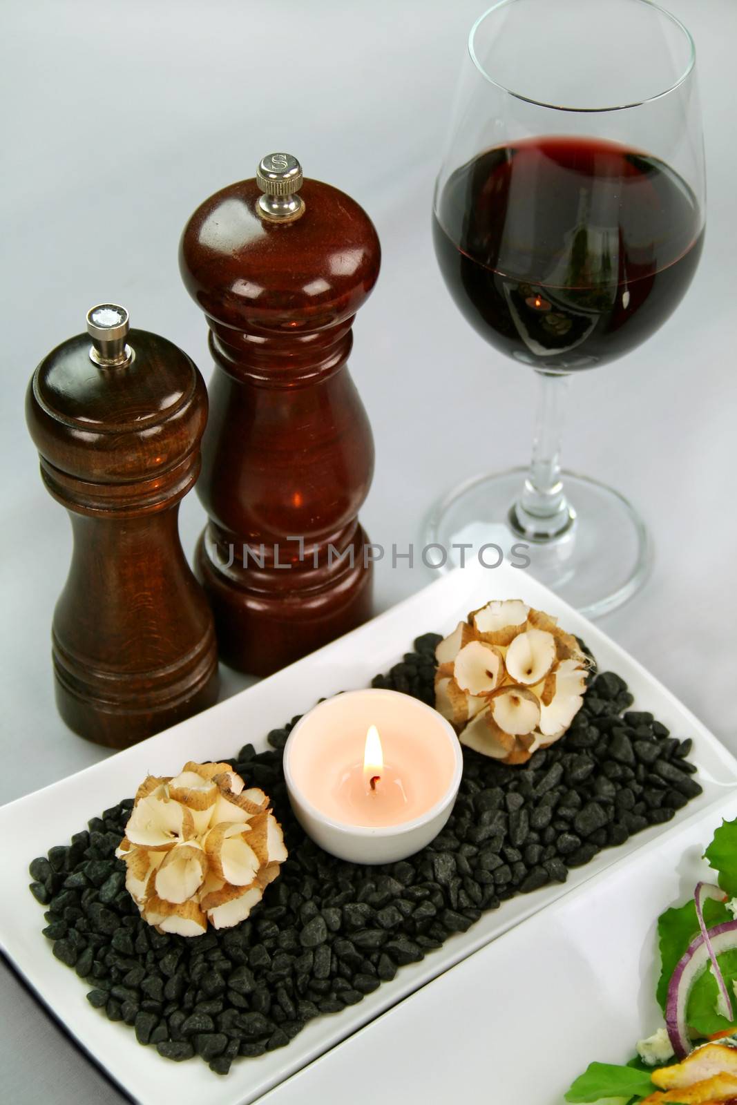 Salt and pepper grinders with a glass of red wine and a tea candle with decorations.