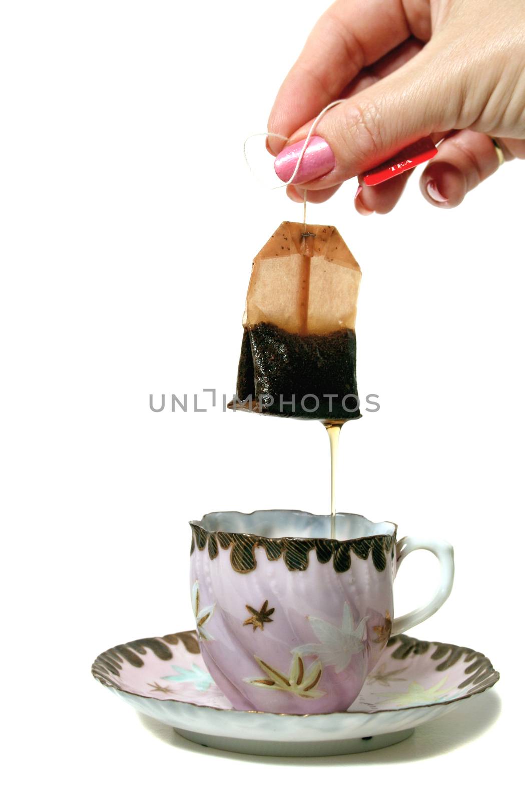 Dripping tea bag held above an antique teacup and saucer.