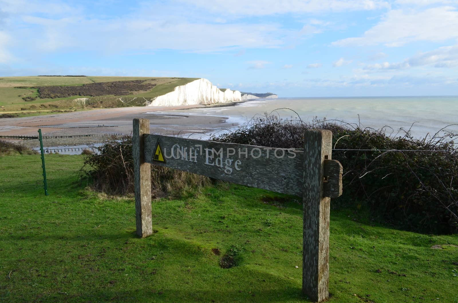 Wooden sign warning of a cliff edge.Image of the Seven Sisters in the background.