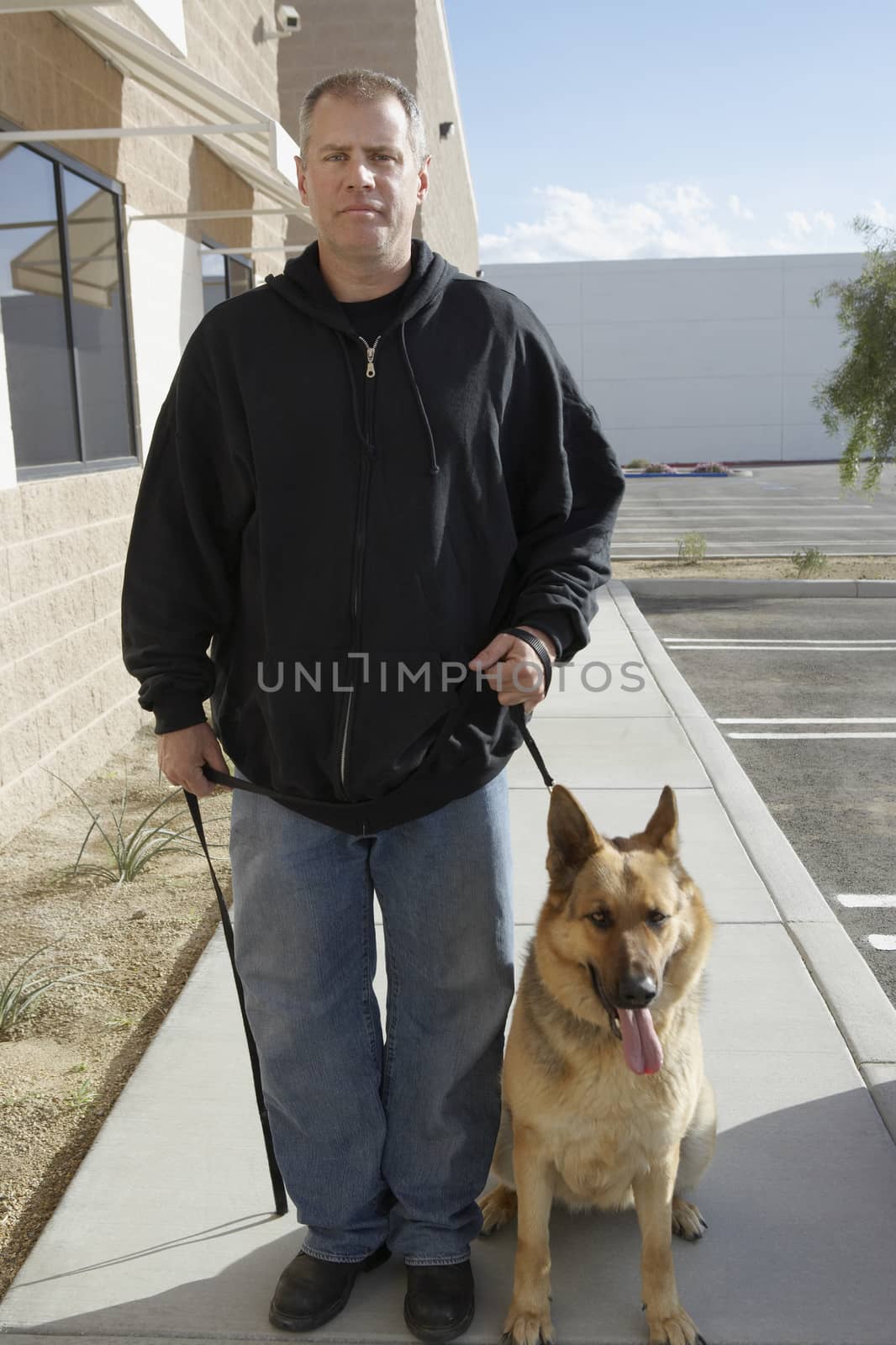 Full length of a security guard standing with trained dog at sidewalk by moodboard