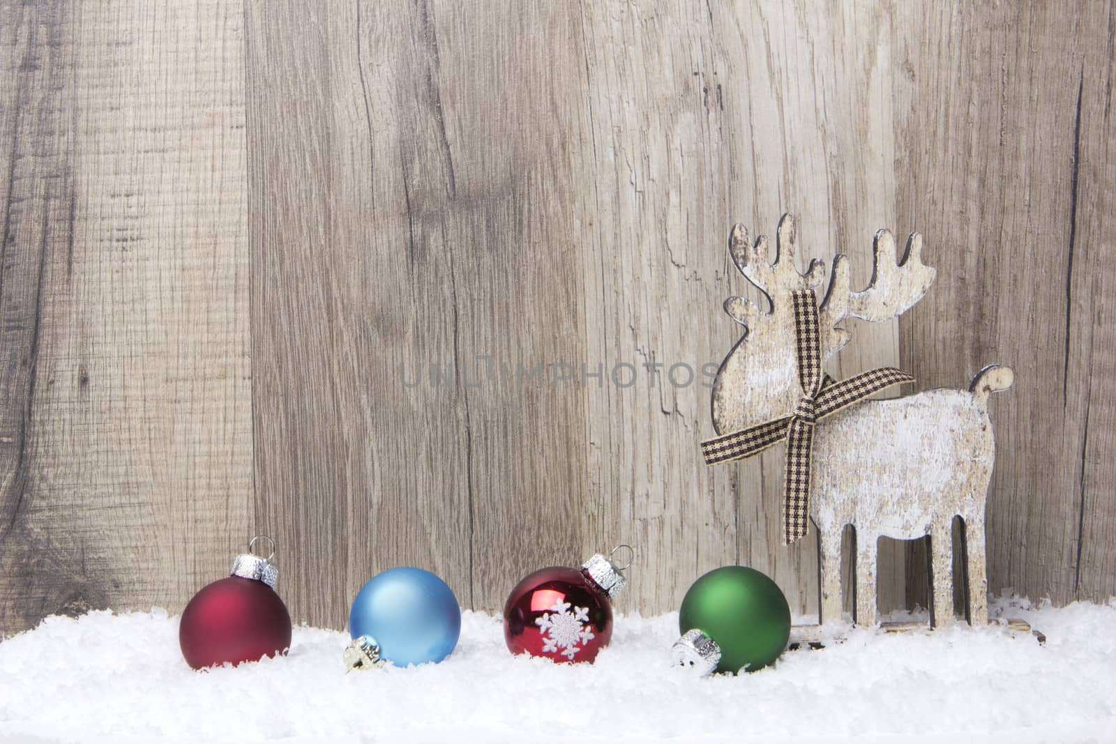 christmas decoration with wood background, snow, elk and christmas baubles red, blue, green