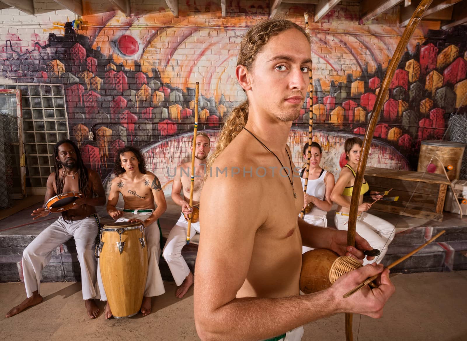 Handsome male capoeira musician with berimbau and group
