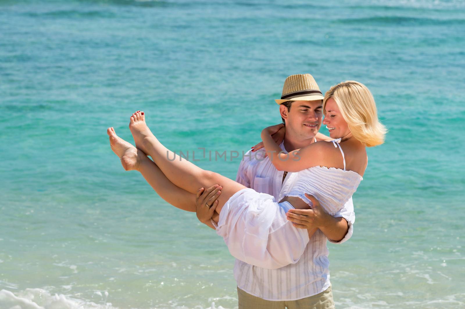 Happy young man carry woman. Couple enjoying at beach with blue sea on background.