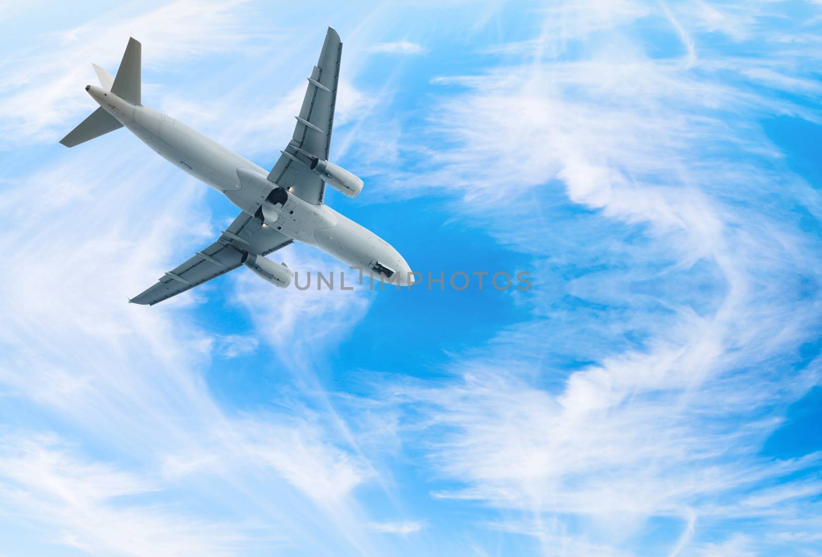 White jet airplane fly in blue bright wispy cloudy blue sky