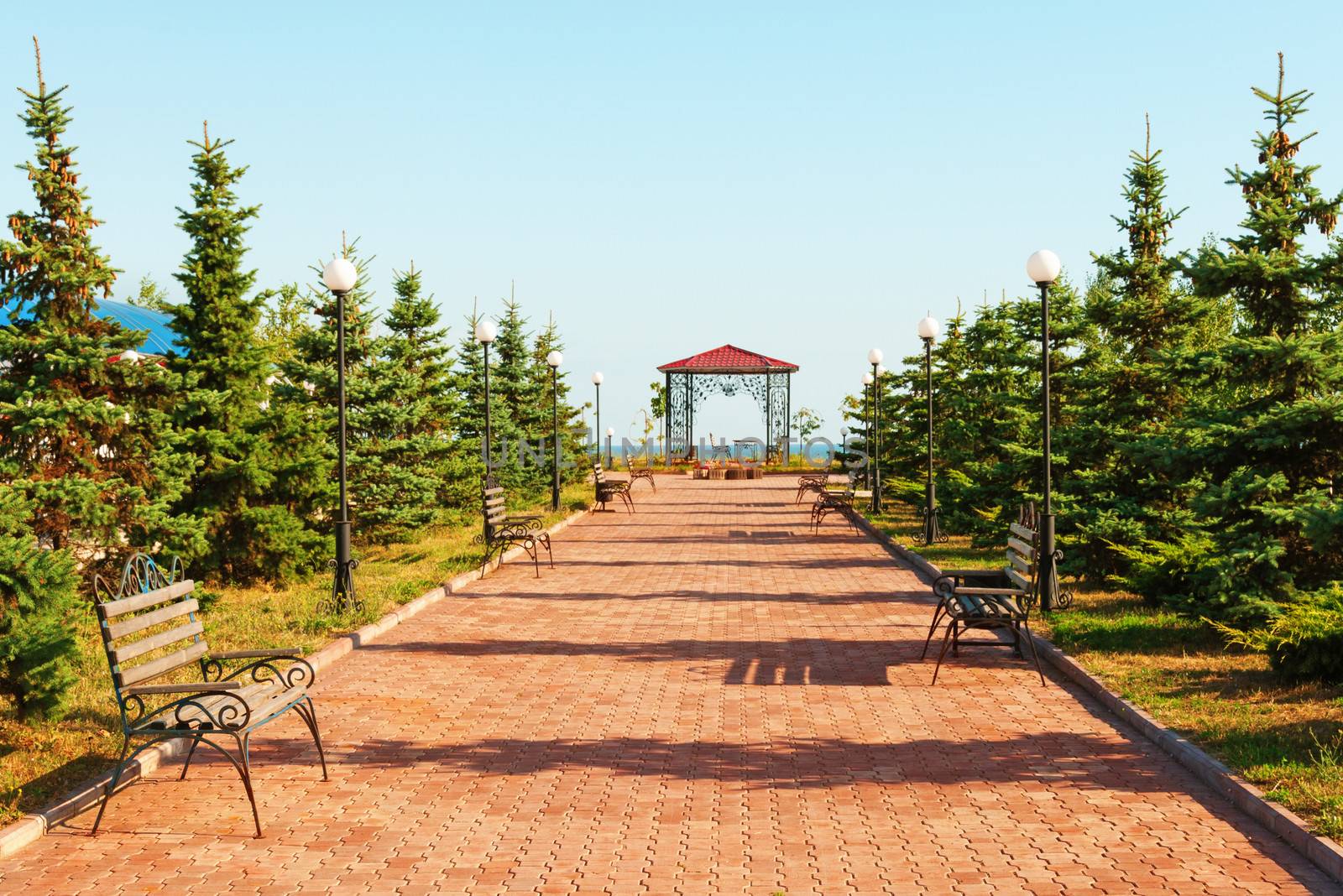 Wide path in nice light  park with benches and summerhouse under clean blue sky