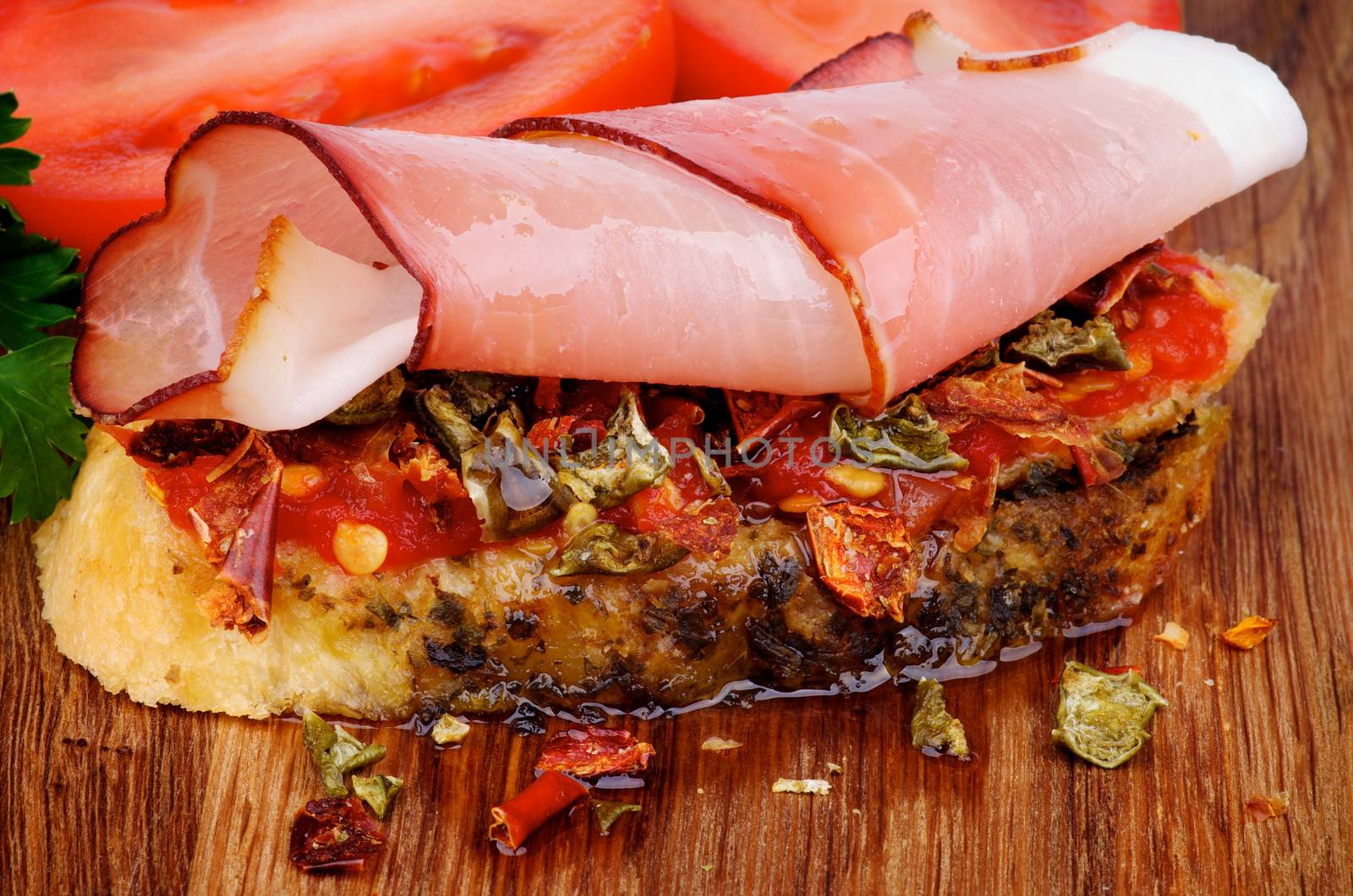 Delicious Spanish Tapas with Cured Ham Prosciutto, Slices of Paprika, Pepper, Toast and Olive Oil closeup on Wooden background