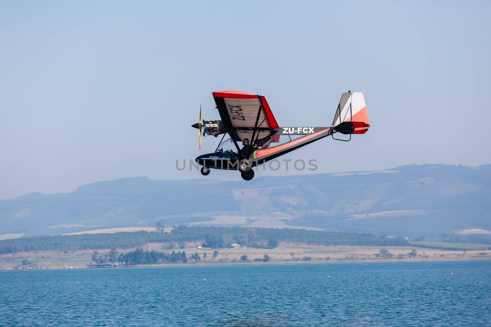 Pilot in light microlight aircraft flying low over dam waters.