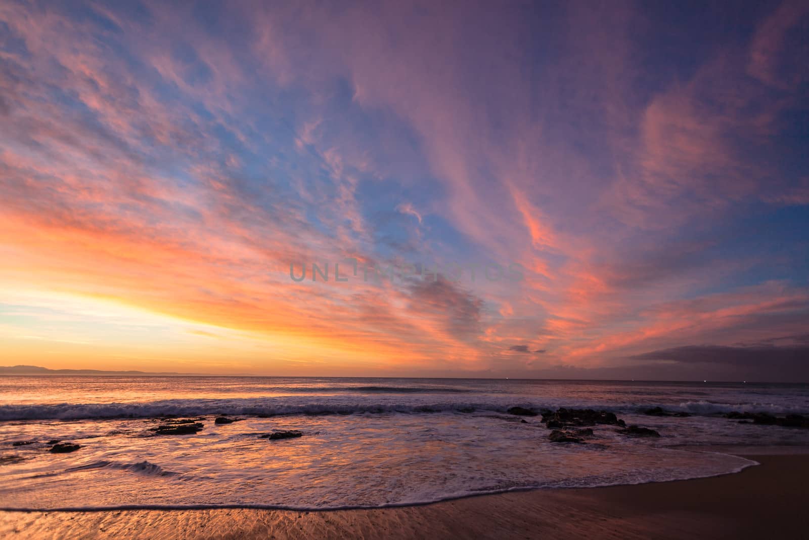 Dawn morning light colors the cirrus clouds blue sky beach ocean waves in amazing color canvas of nature for a moment.
