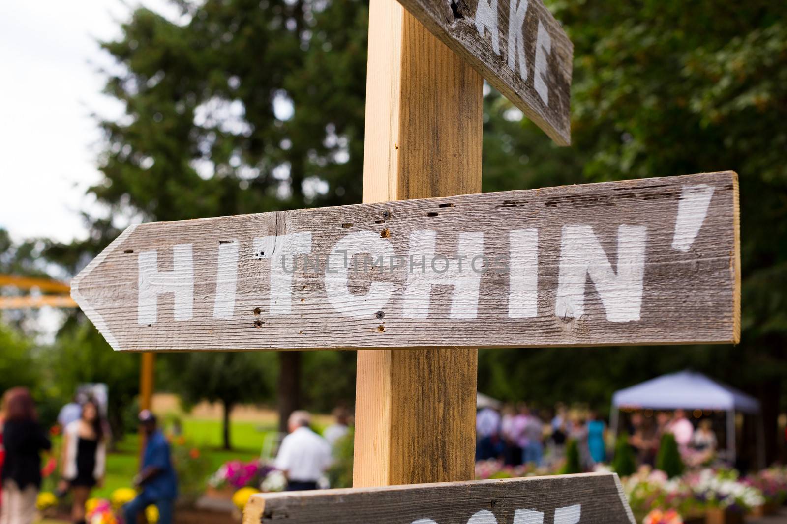 A handmade sign reads hithcin at an outdoor summer wedding pointing guests to the ceremony location.