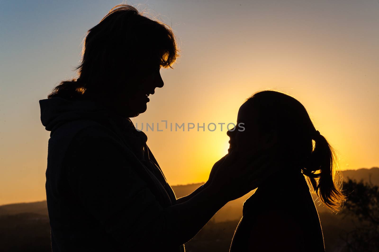 Mother daughter affection caring moments together silhouetted outlines at sunset.
