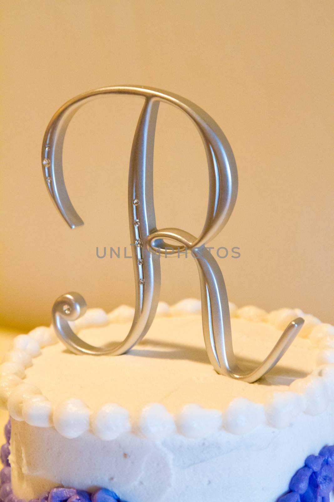 A cake topper with the letter R on it on this white and purple cake indoors.