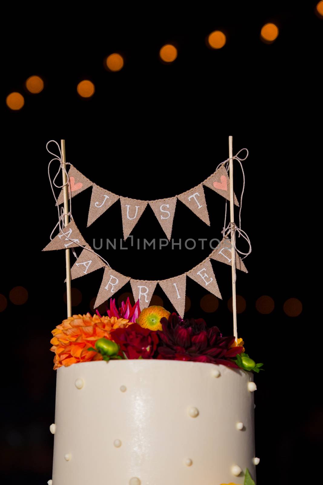 A handmade cake topper has flags that say just married on it above the wedding cake at this reception party.