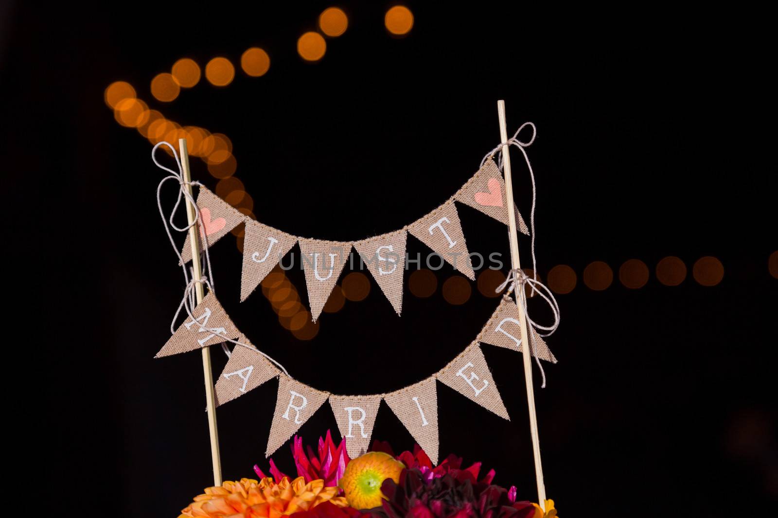 A handmade cake topper has flags that say just married on it above the wedding cake at this reception party.