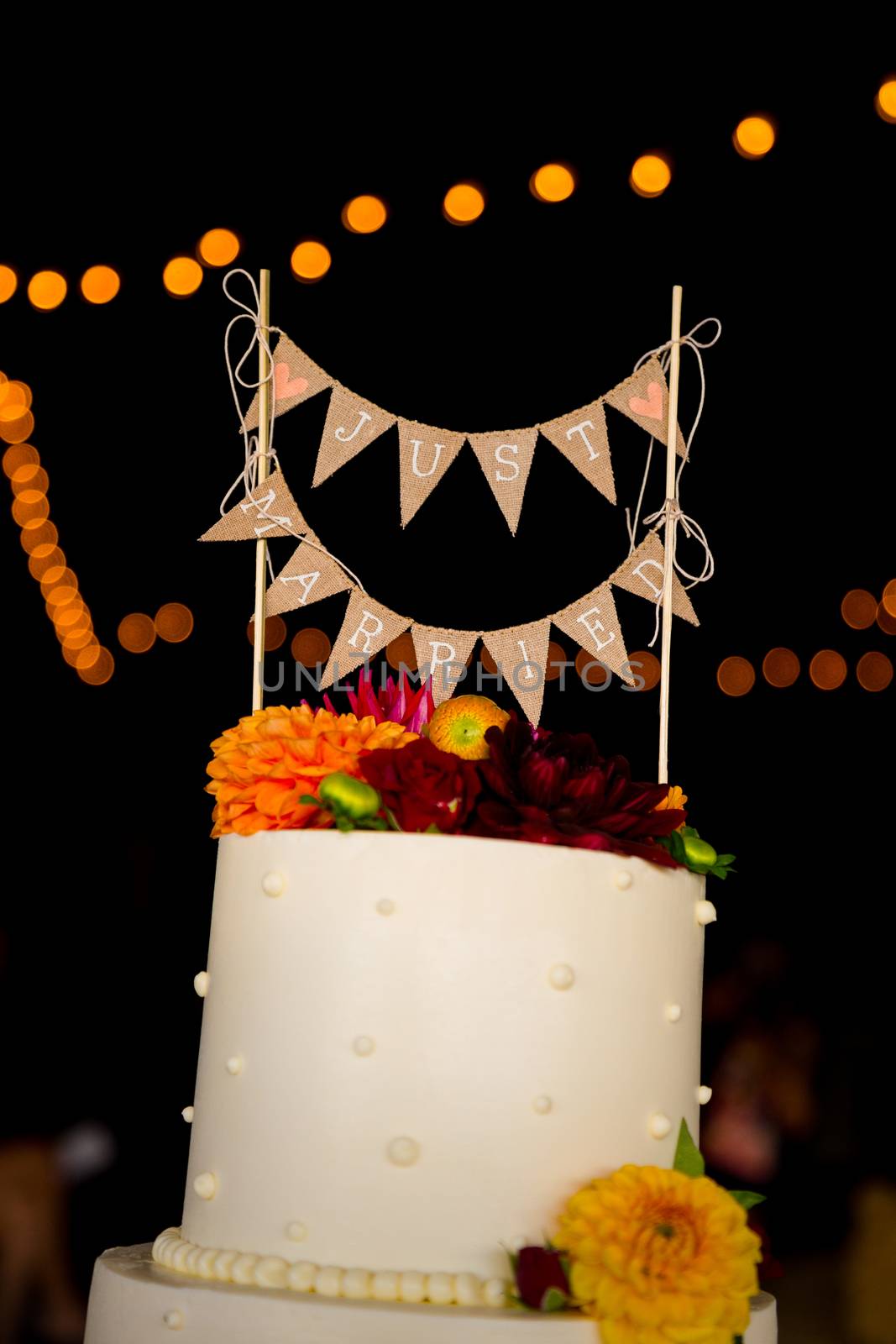 A handmade cake topper has flags that say just married on it above the wedding cake at this reception party.