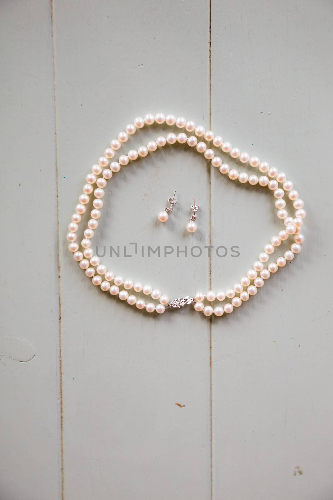 A pearl neckalce and some earrings are waiting on the table for the bride to finish getting ready and put on her jewelry.