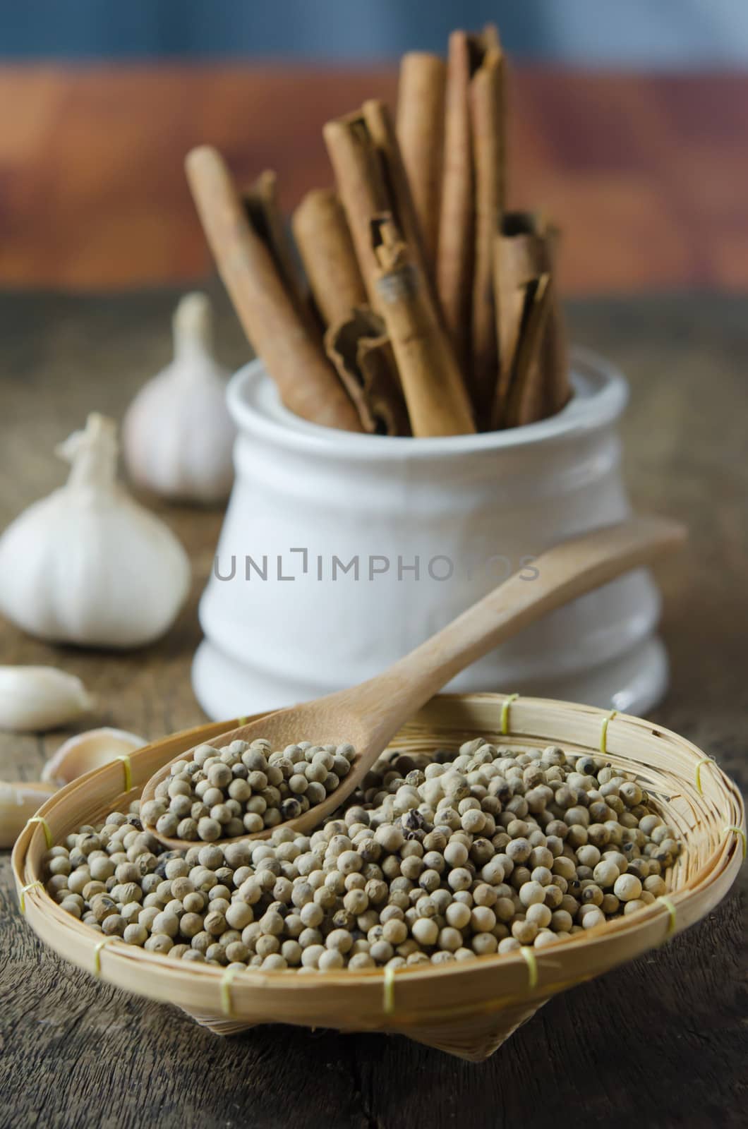 close up  peppercorns on basket with spoon and cinnamon sticks in bowl , garlic over wooden background